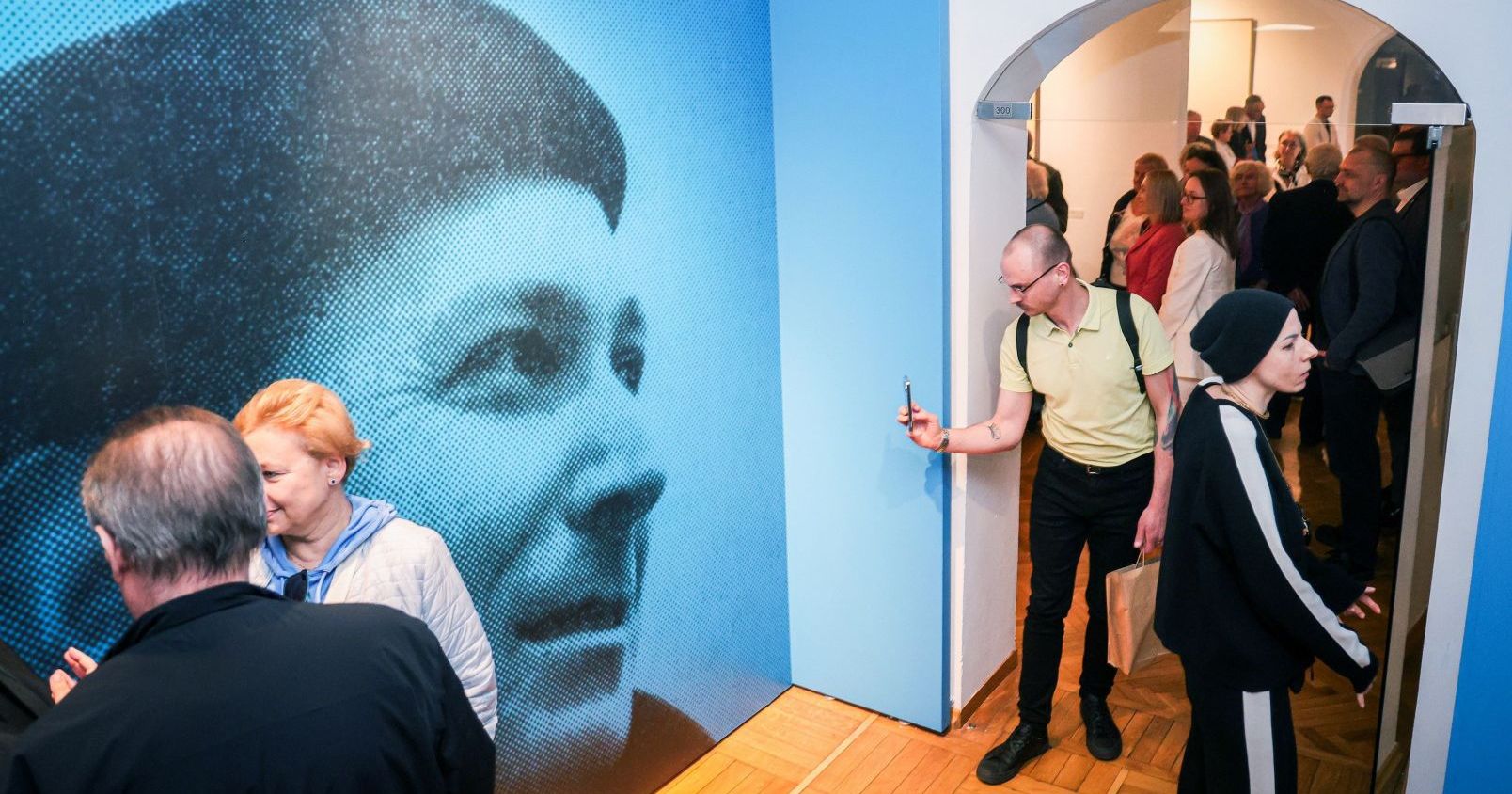 Fragment wystawy - z lewej strony portret malarza na całą ścianę, z prawej tłum zwiedzających