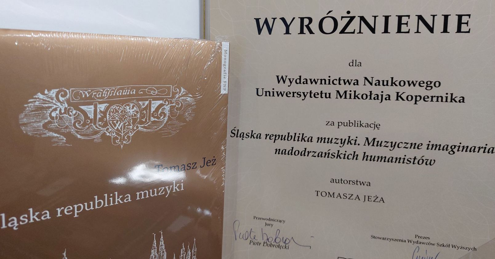 Rozstrzygnięcie konkursu nastąpiło 7 marca podczas uroczystego otwarcia Poznańskich Targów Książki Zdjęcie fragmentu okładki książki po lewej stronie zdjęcia, po prawej dyplom