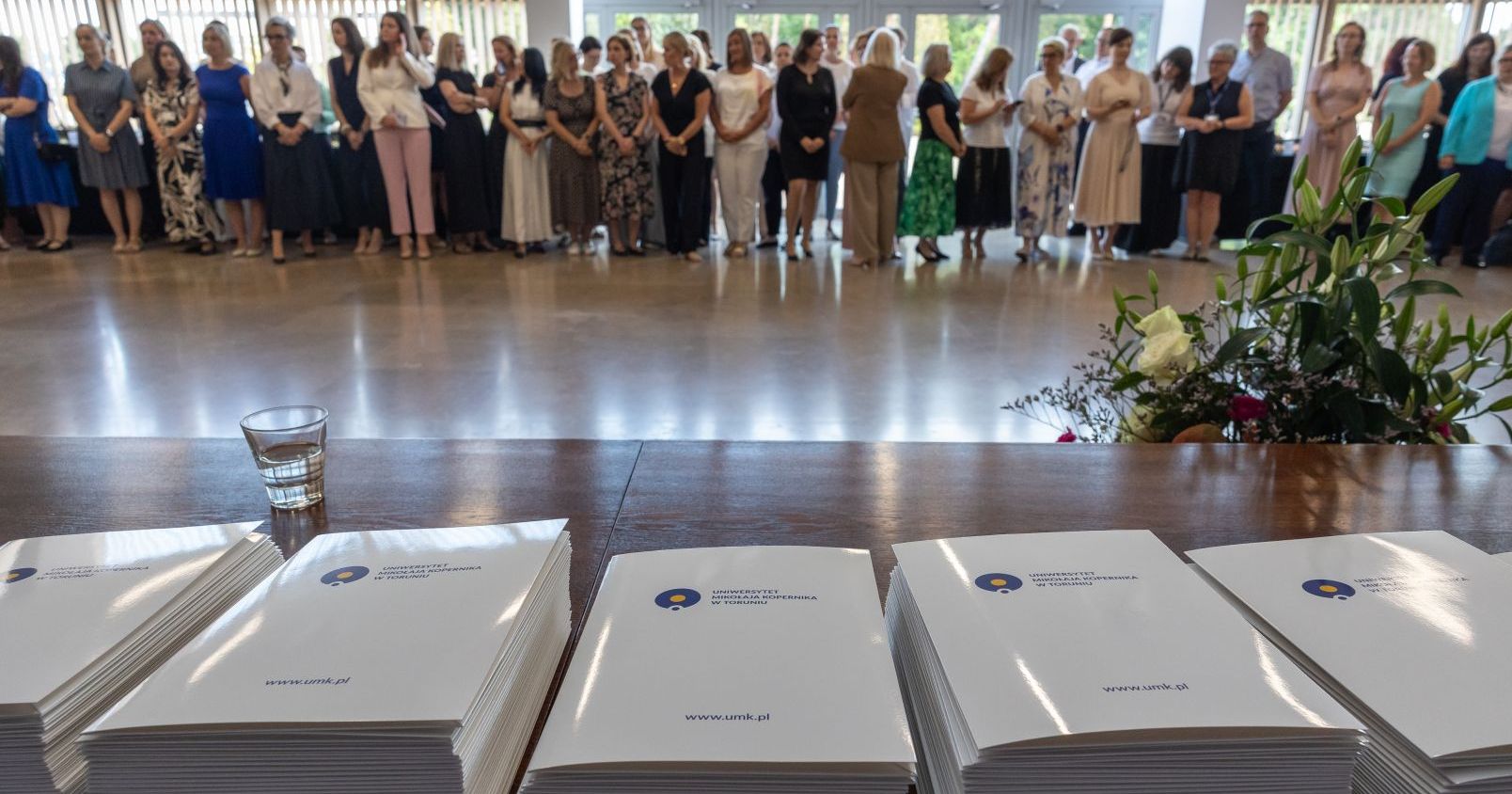 - Jestemy postrzegani jako jeden z najlepszych uniwersytetów w Polsce, a pod względem wysokości subwencji jesteśmy siódmą uczelnią w kraju - mówił rektor prof. Andrzej Tretyn podczas uroczystości w Auli UMK Na pierwszym planie teczki z logiem UMK, w tle grupa osób czekających na odbiór nagrody