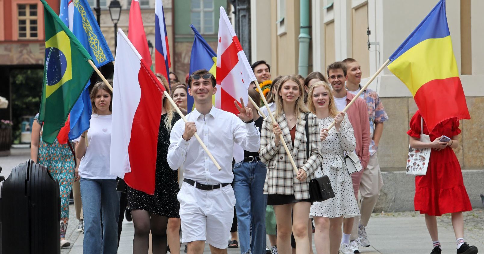  Zdjęcie przedstawia grupę ludzi, która idzie w kierunku fotografia, trzymając duże flagi różnych państw.