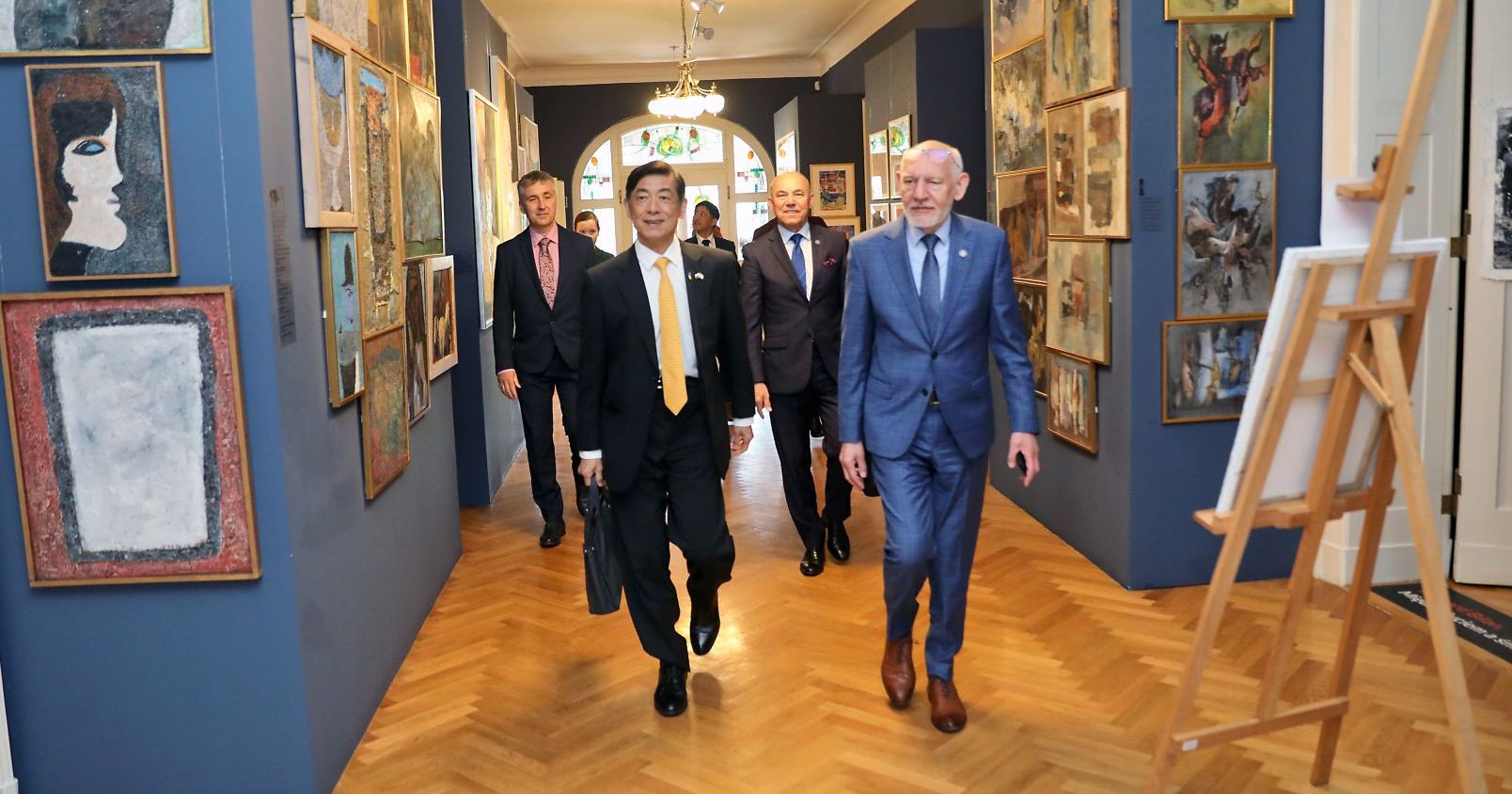  Ambasador Japonii oraz Rektor UMK idący przez korytarz. Na drugim planie prorektor Wojciech Wysota i pozostali uczestnicy spotkania.