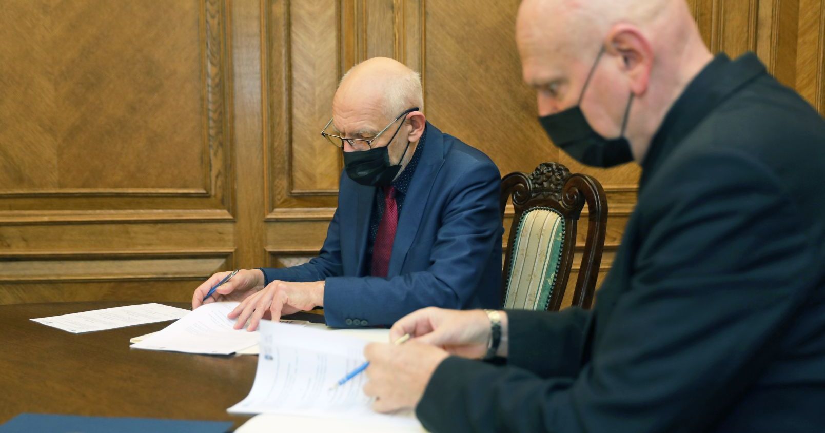 Porozumienie podpisali rektor UMK prof. dr hab. Andrzej Sokala i prezydent Torunia Michał Zaleski Dwóch mężczyzn siedzą przy stole i podpisują dokumenty, mężczyźni są w maseczkach