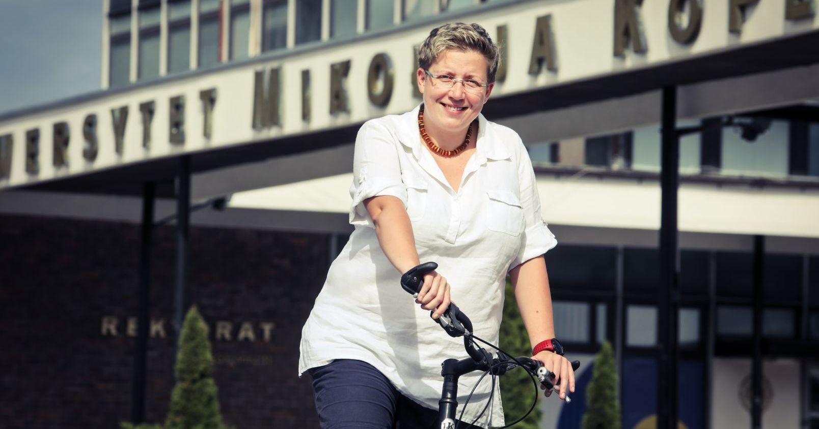 Dr Anna Dubownik, koordynatorka ds. Społecznej Odpowiedzialności Uczelni na UMK Kobieta na rowerze, za nią budynek rektoratu UMK