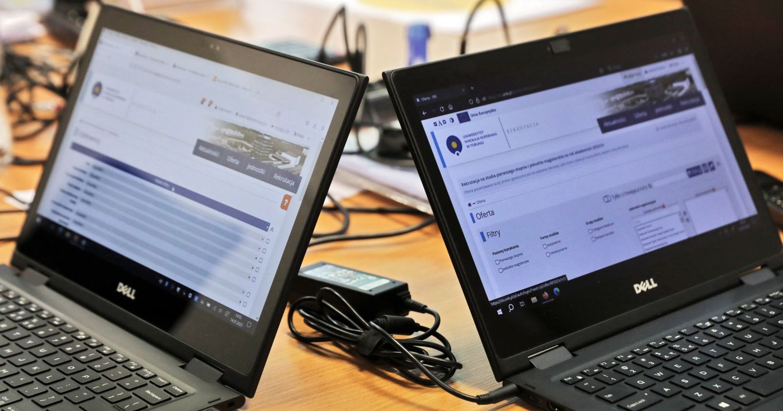 Dwa czarne lapotopy stoją na stole, wokół kable, na ekranach strony internetowej rejestracji kandydatów na UMK