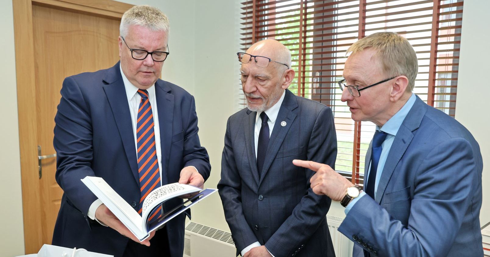 Trzech mężczyzn rozmawia, jeden trzyma otwartą książkę