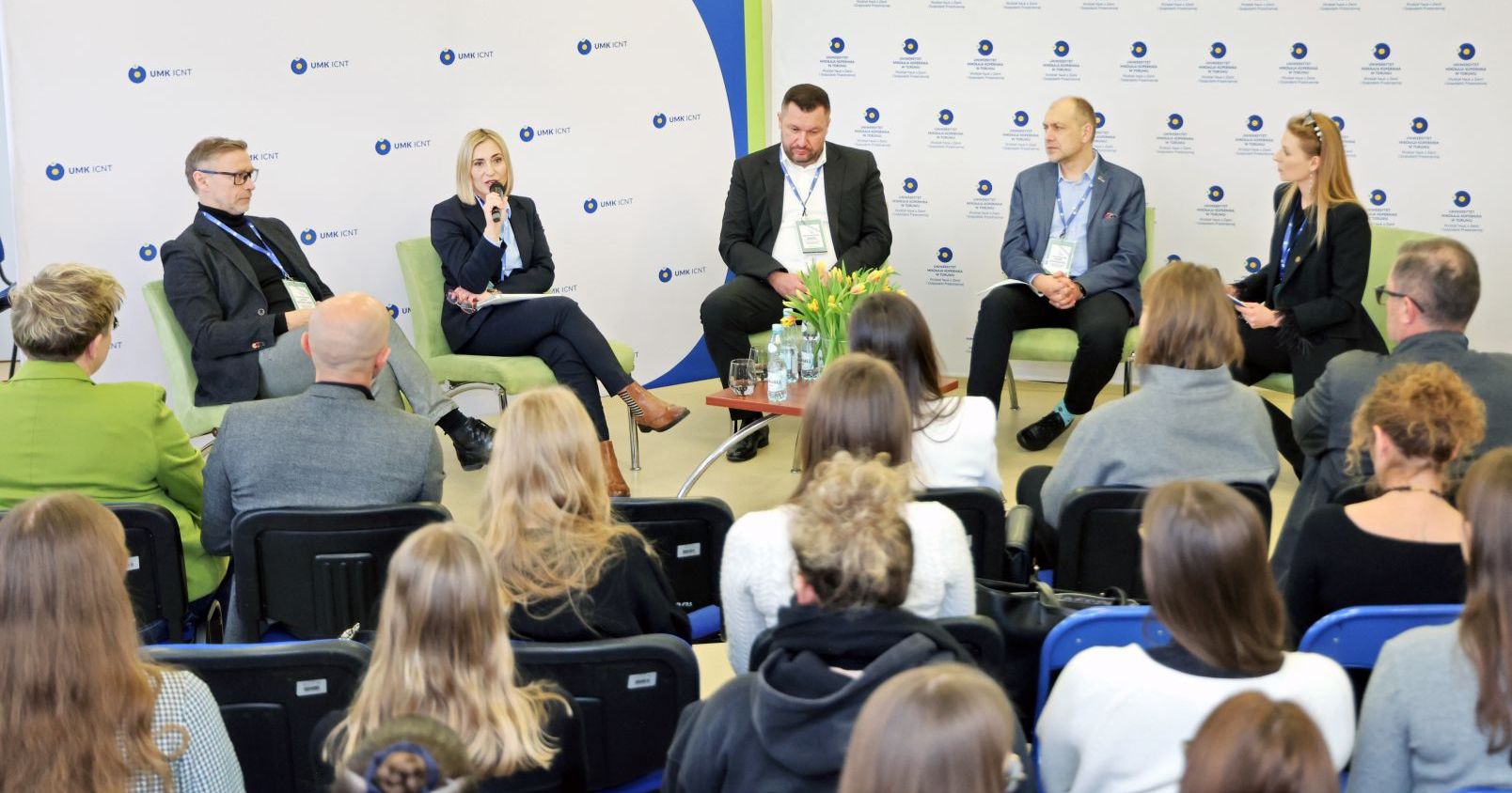 Na tle ścianek promocyjnych umk siedzą od lewej Marcin Drogorób, Karolina Sokalska, Michał Michalski, Konrad Nowakowski i dr Anna Michalska. Na pierwszym planie siedząca tyłem do fotografa publiczność