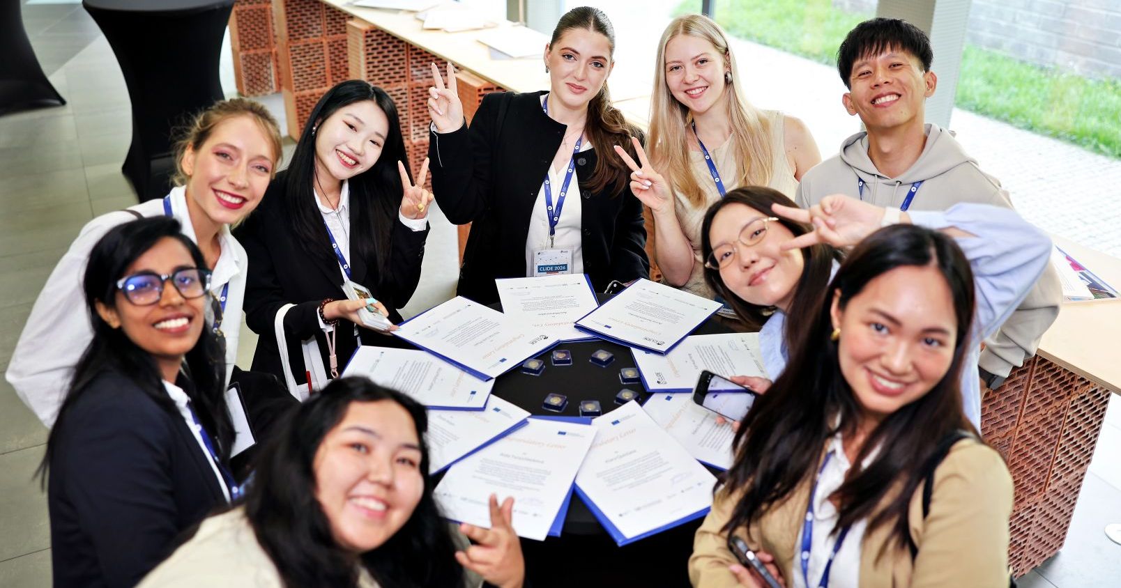 Nine international students are sitting at a round table and smiling at the camera