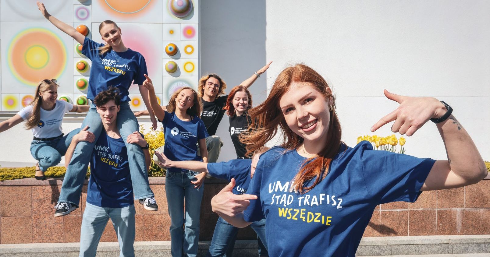 Rekrutacji na UMK towarzyszy hasło "Stąd trafisz wszędzie!", które podkreśla, że studia na UMK otwierają drzwi do kariery, realizowania ambicji, aspiracji i spełniania marzeń. Grupka uśmiechniętych studentów i studentek w koszulkach z hasłem "UMK stąd trafisz wszędzie", w tle mozaika Stefana Knappa zdobiąca fasadę Auli UMK