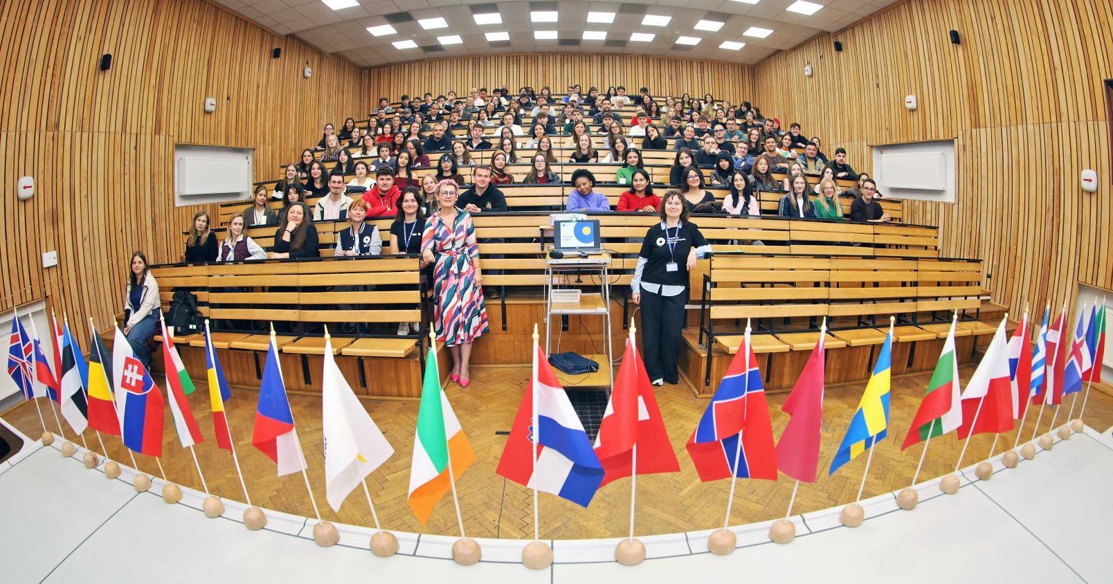 Sala wykładowa, w której siedzą studenci zagraniczni, na pierwszym planie kolorowe flafi róznych krajów