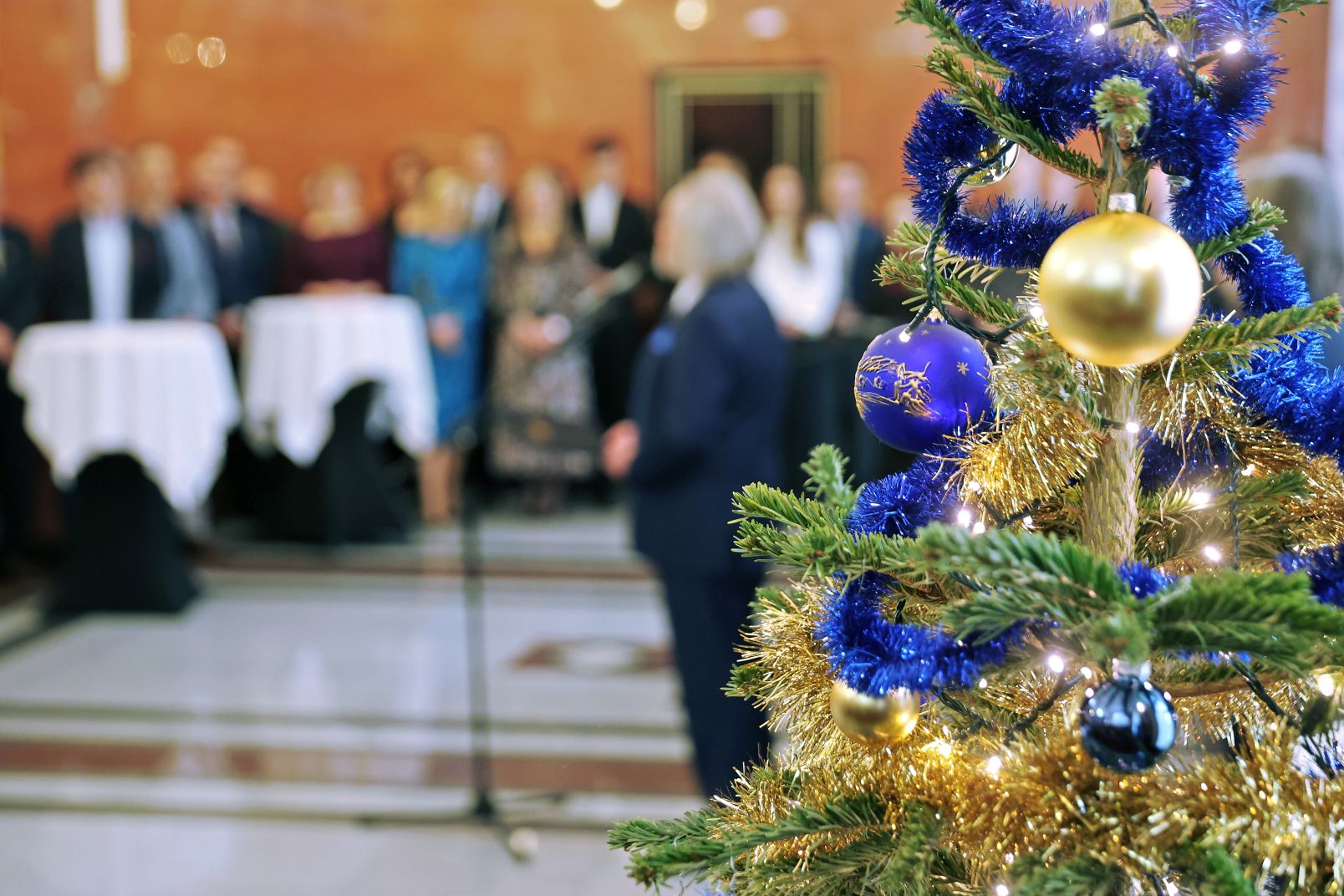 A decorated Christmas tree with blurred participants of the meeting in the background.