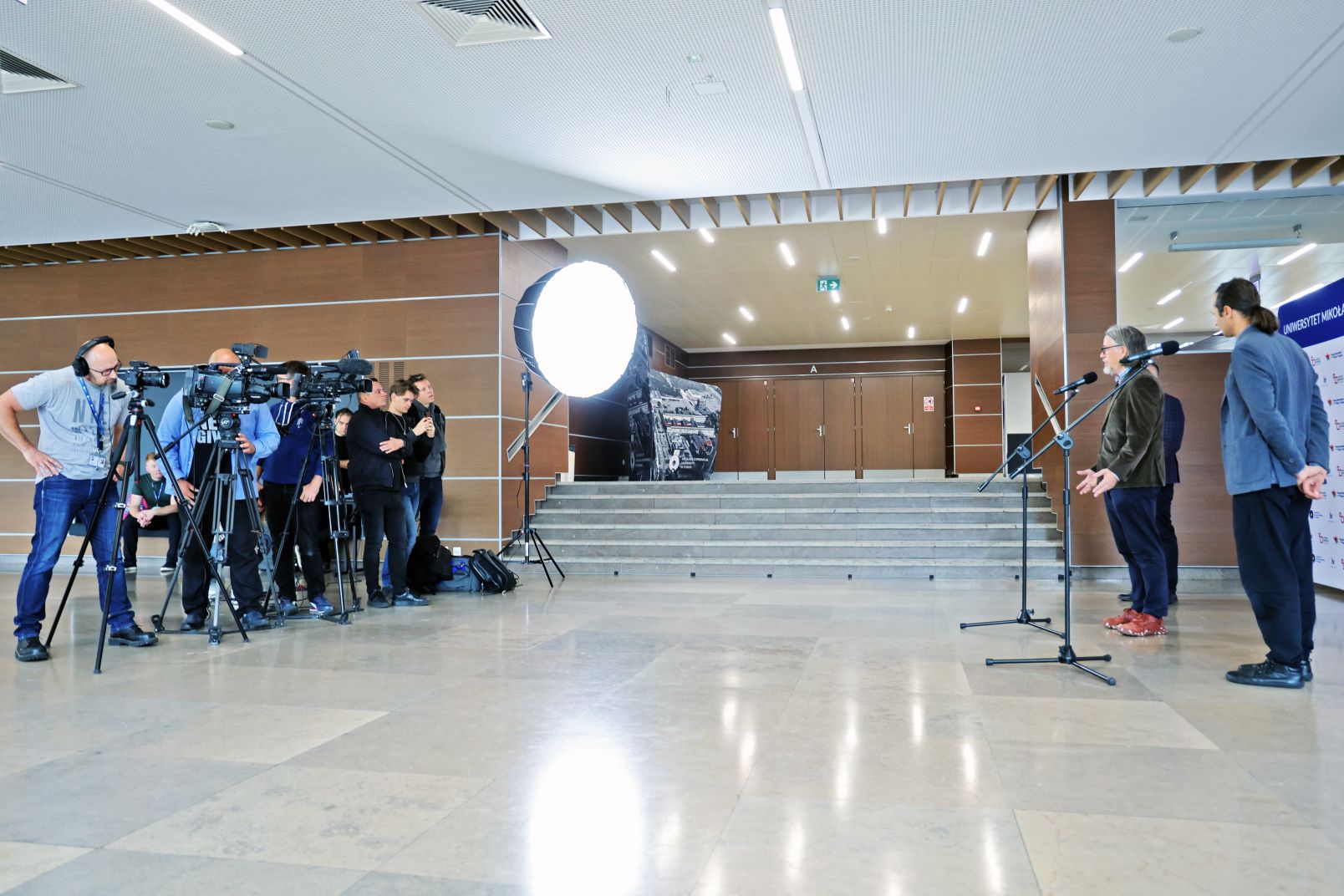 Dziennikarze z kamerami telewizyjnymi stoją na konferencji prasowej w auli UMK