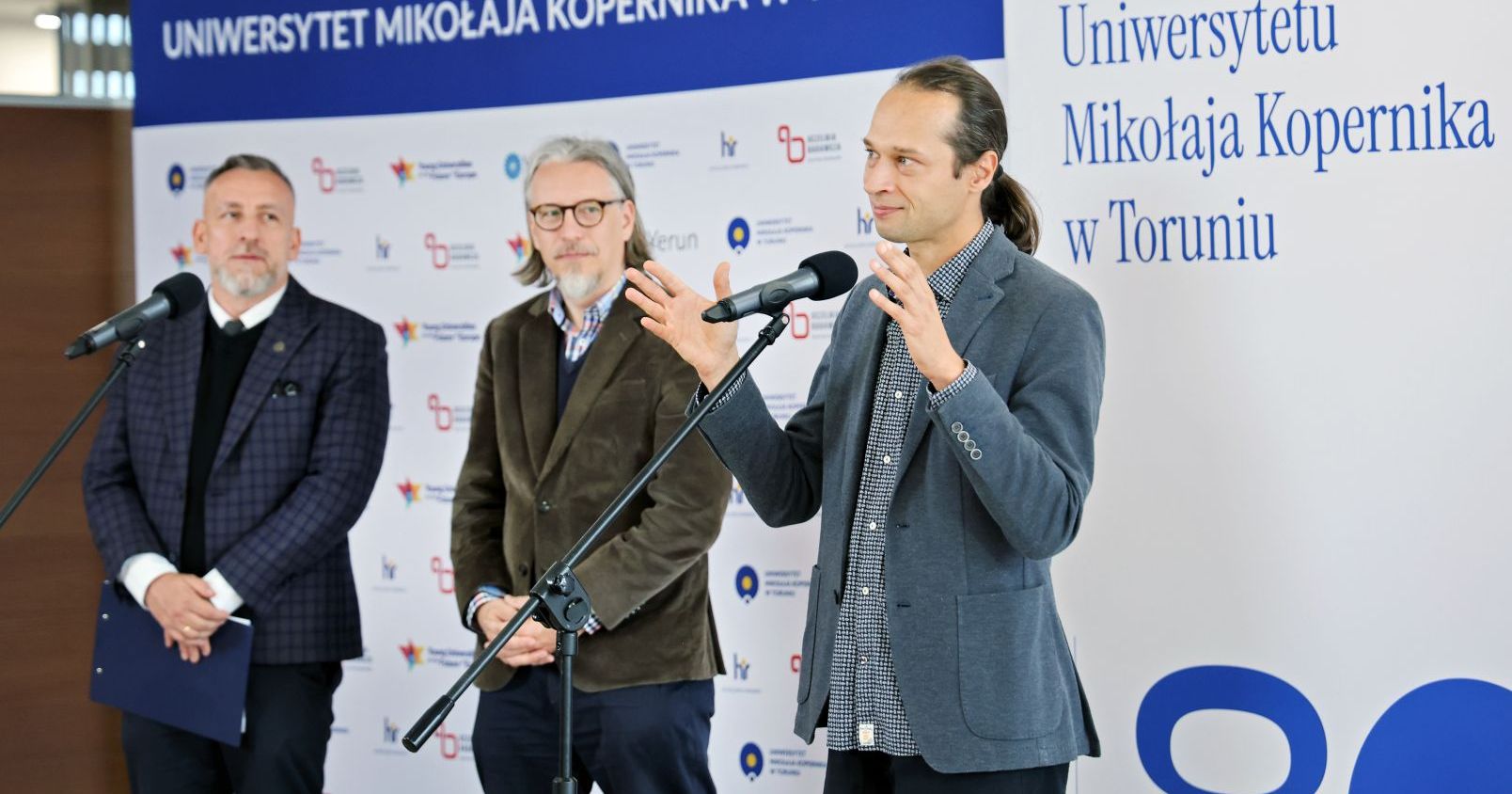 Rozpoczęciu projektu towarzyszyła konferencja prasowa w Auli UMK Trzech mężczyzn stoi na tle ścianki promocyjnej UMK. Przed nimi mikrofony na statywach. Jeden z mężczyzn żywiołowo gestykuluje
