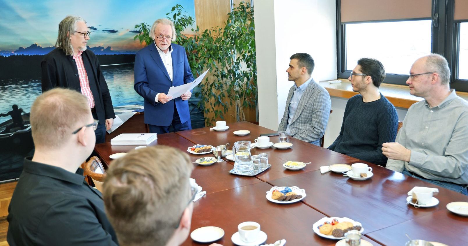Five men are sitting at the table. Two people are also standing by it: the university rector and the vice-rector