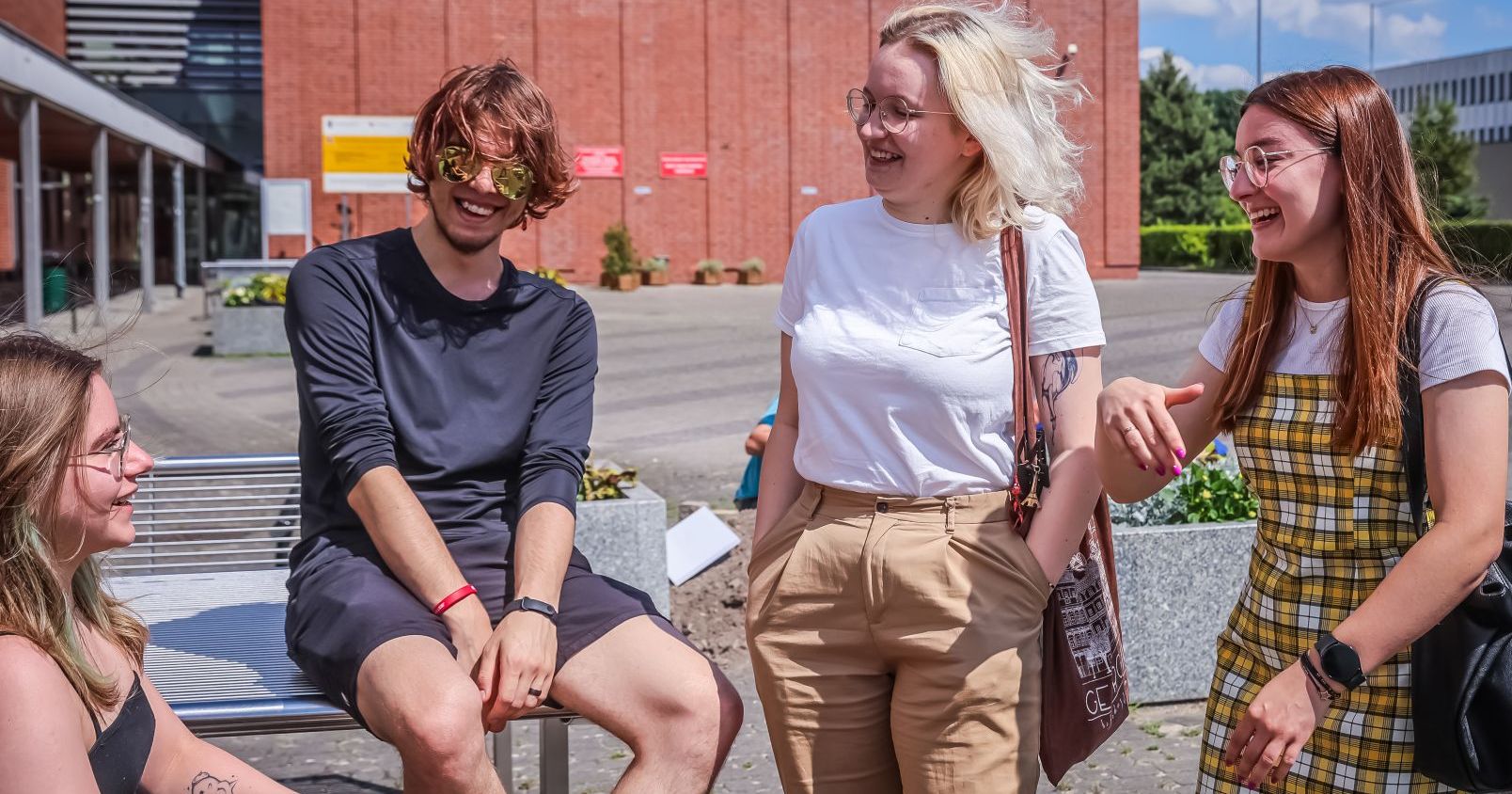 Czworo uśmiechniętych studentów przed budynkiem z czerwonej cegły