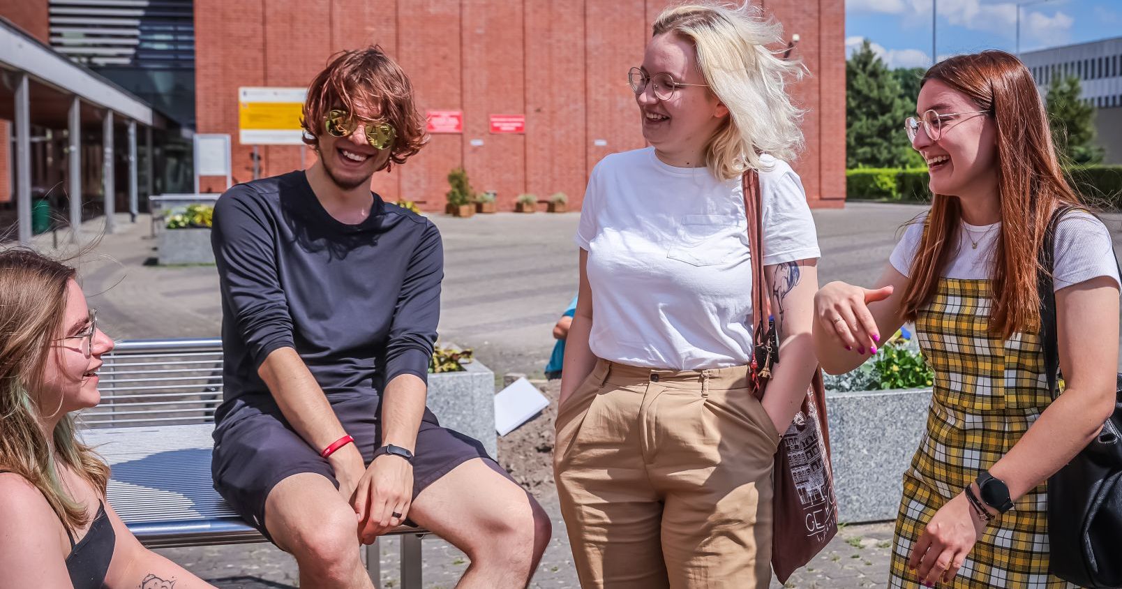 Four smiling students in front of a red brick building