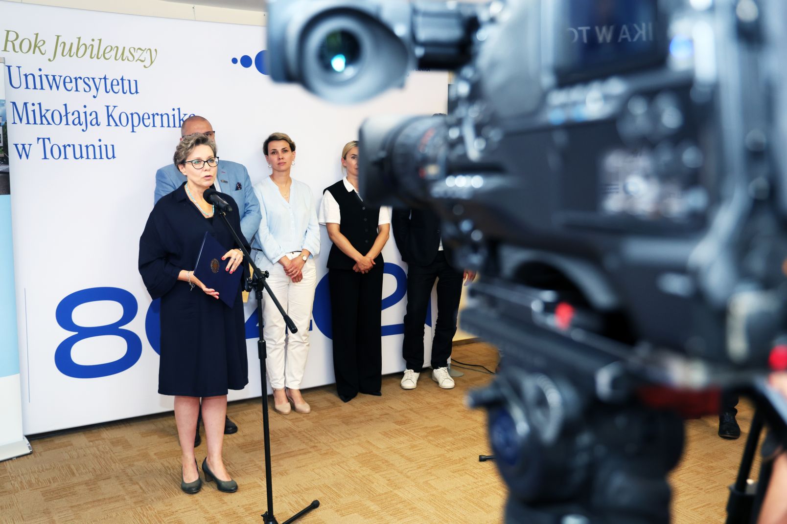 Prof. Joanna Kucharzewska przemawia do mikrofonu, na pierwszym planie widać kamerę