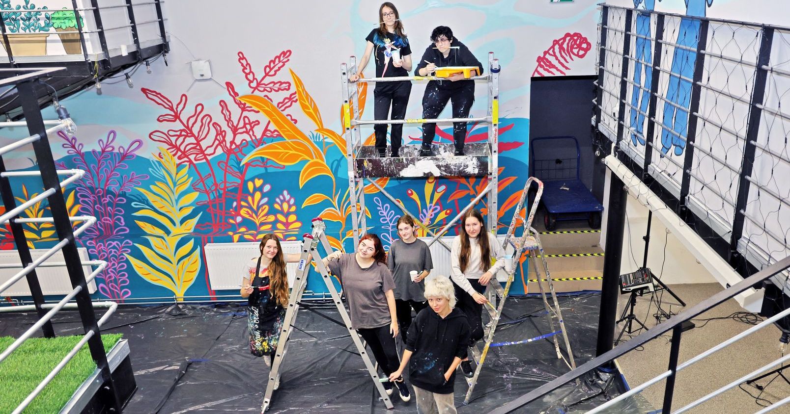Seven people involved in painting the mural in front of their work, scaffolding and ladders still visible.