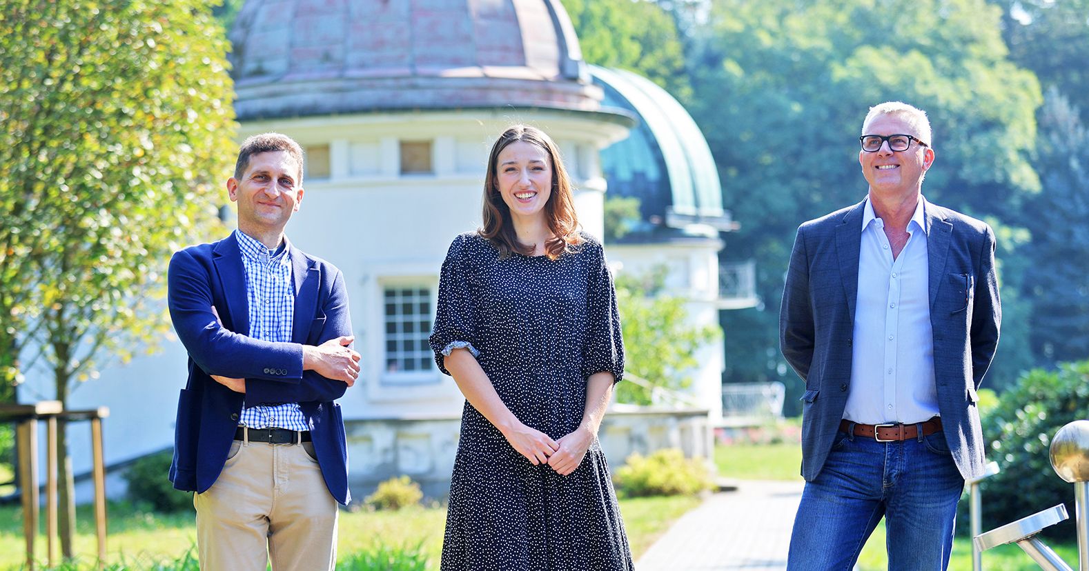 Dr hab. Gracjan Maciejewski, prof. UMK, Julia Sierzputowska studentka astronomii oraz prof. dr hab. Andrzej Niedzielski. Dwóch mężczyzn i kobieta stoją na tle astronomicznego pawilonu obserwacyjnego