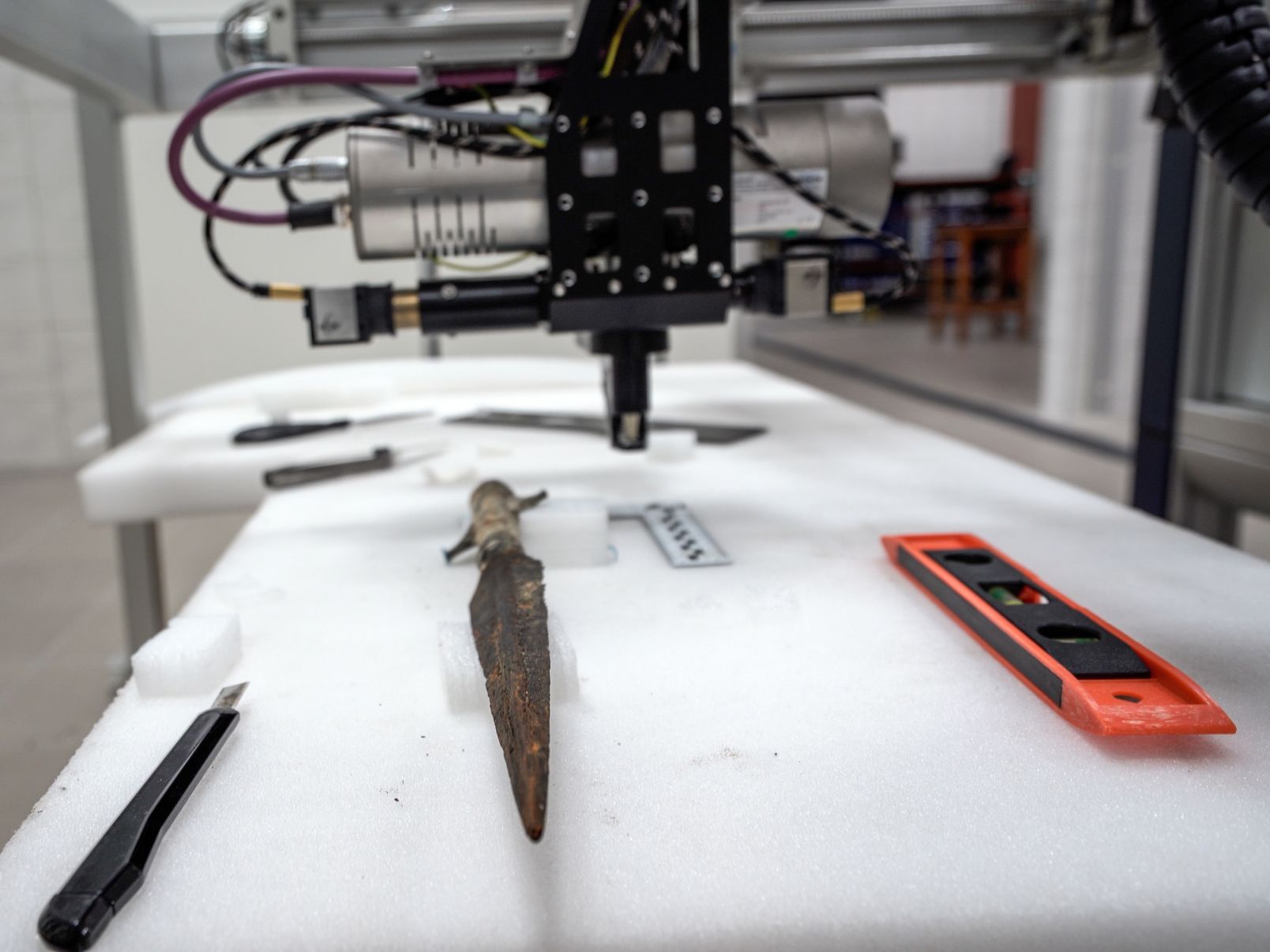 Badanie grotu misternie zdobionej włóczni, na stole obok grotu leżą miarka, poziomica i nożyk