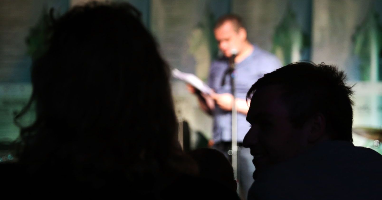  Sylwetki dwóch osób na tle sceny w Od Nowie, na której poeta prezentuje swoje wiersze