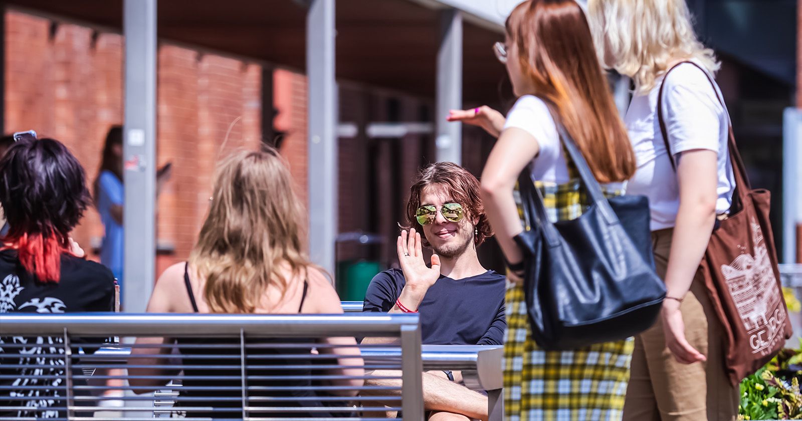 Grupa studentów rozmawia ze sobą przed Wydziałem Humanistycznym. Jeden student patrzy w obiektyw i macha