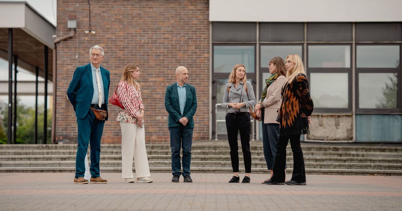 A tour of the modernist campus of Nicolaus Copernicus University in Bielany was one of the items on the agenda during the visit of the Vinci delegation Six people are standing in relaxed poses in front of the rector's office building, chatting.