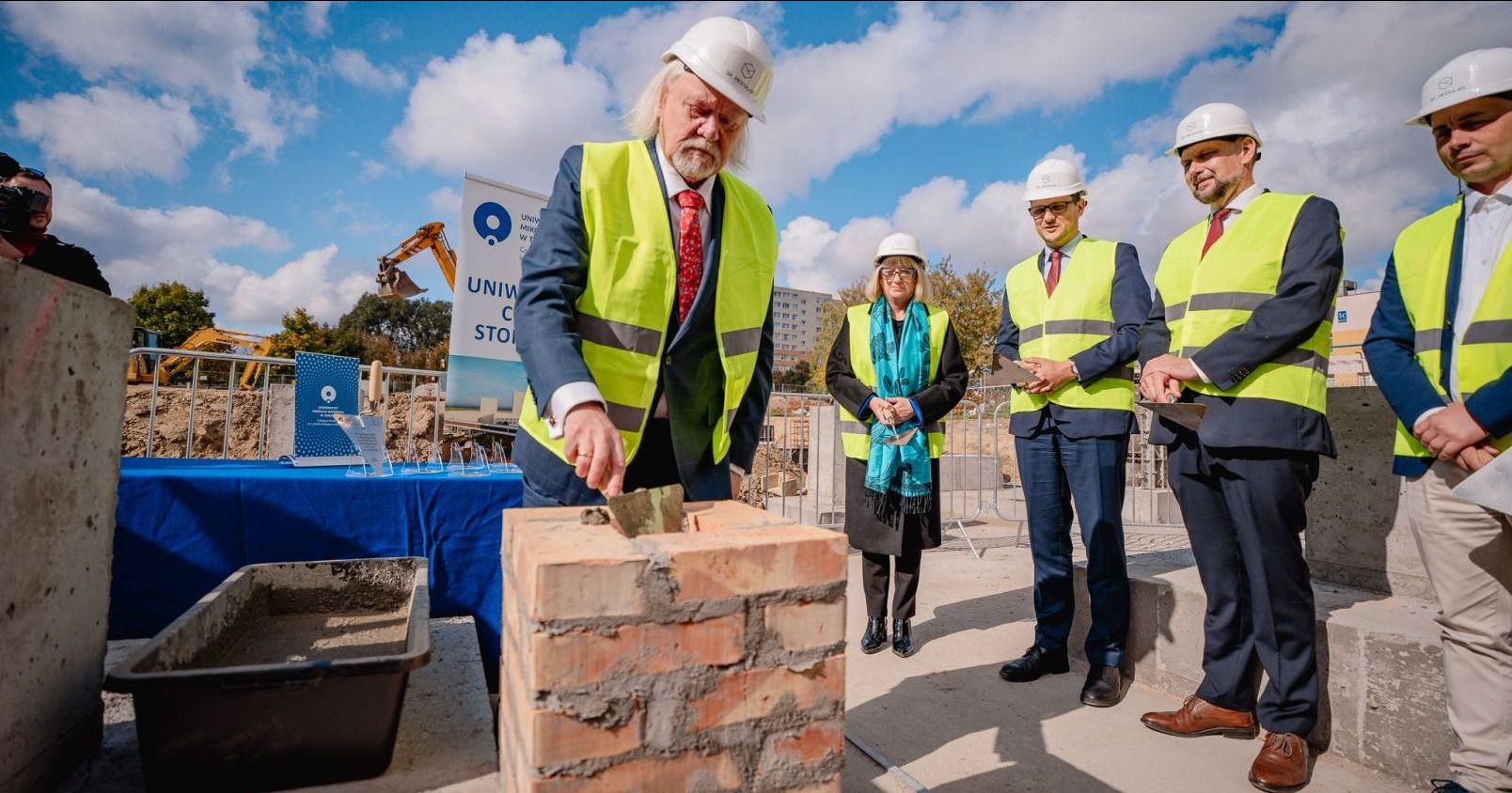 The Rector of Nicolaus Copernicus University, Prof. Andrzej Tretyn, holding a trowel, lays the cornerstone document at the construction site