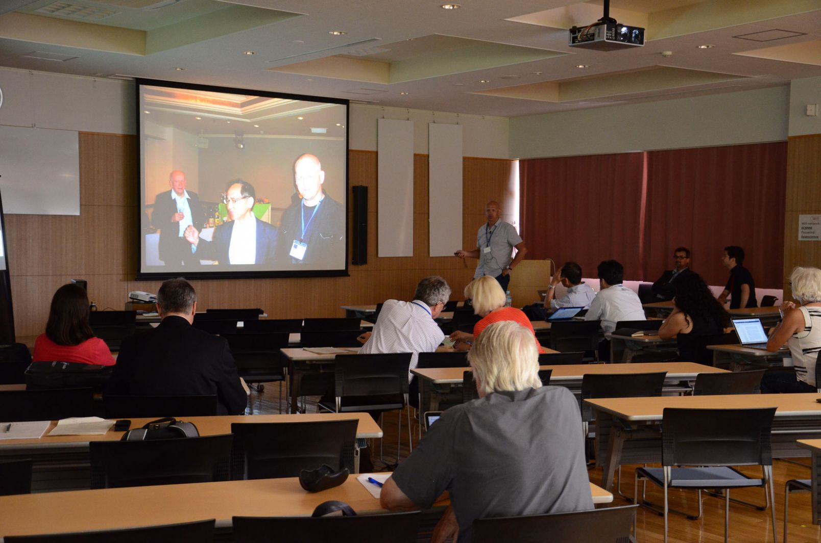 Wykład prof. Terzyka na organizowanych w Japonii w 2017 r. spotkaniu poświęconemu nanomateriałom. Ludzie siedzący na sali i ekran rzutnika w tle.