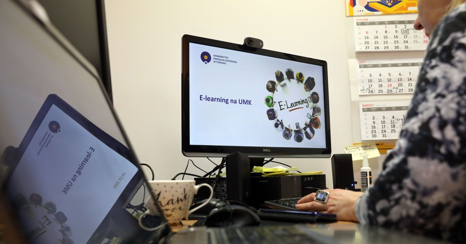 Łącznie na przygotowanie e-learnigowych kursów akademickich UMK otrzyma ponad 780 tys. zł Osoba siedzi przy biurku, na monitorze wyświetlona jest grafika z napisem "E-learning na UMK"