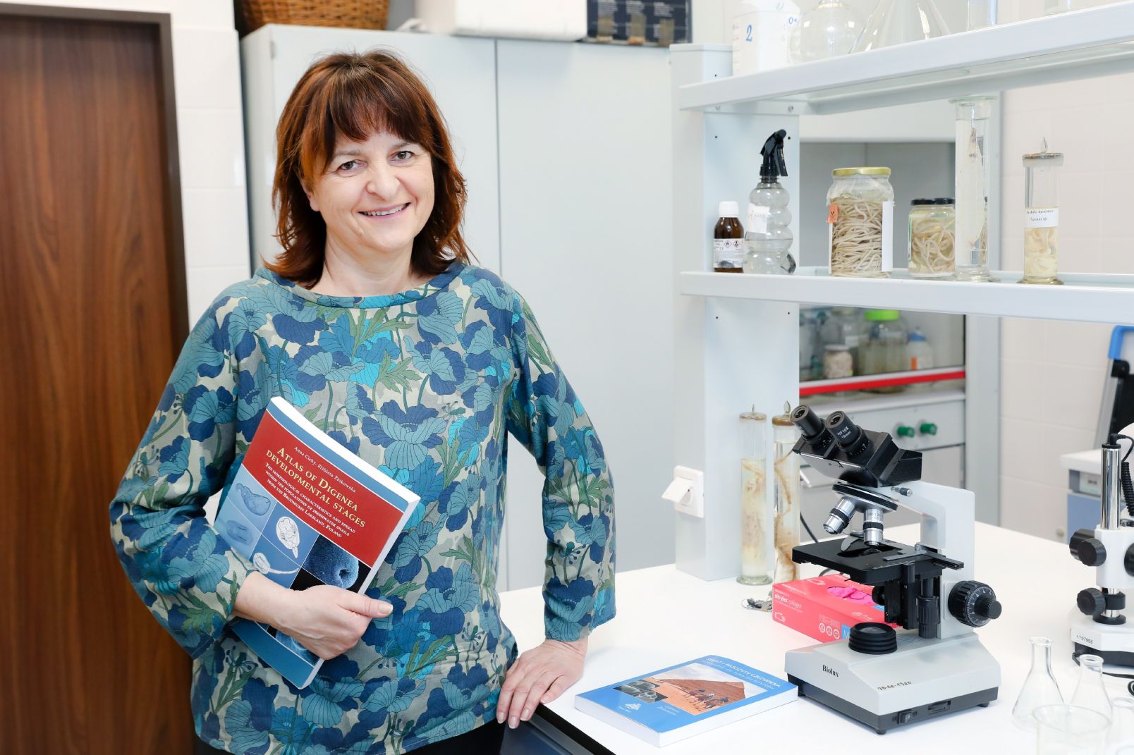 Prof. dr hab. Elżbieta Żbikowska stoi w laboratorium z książką w ręku