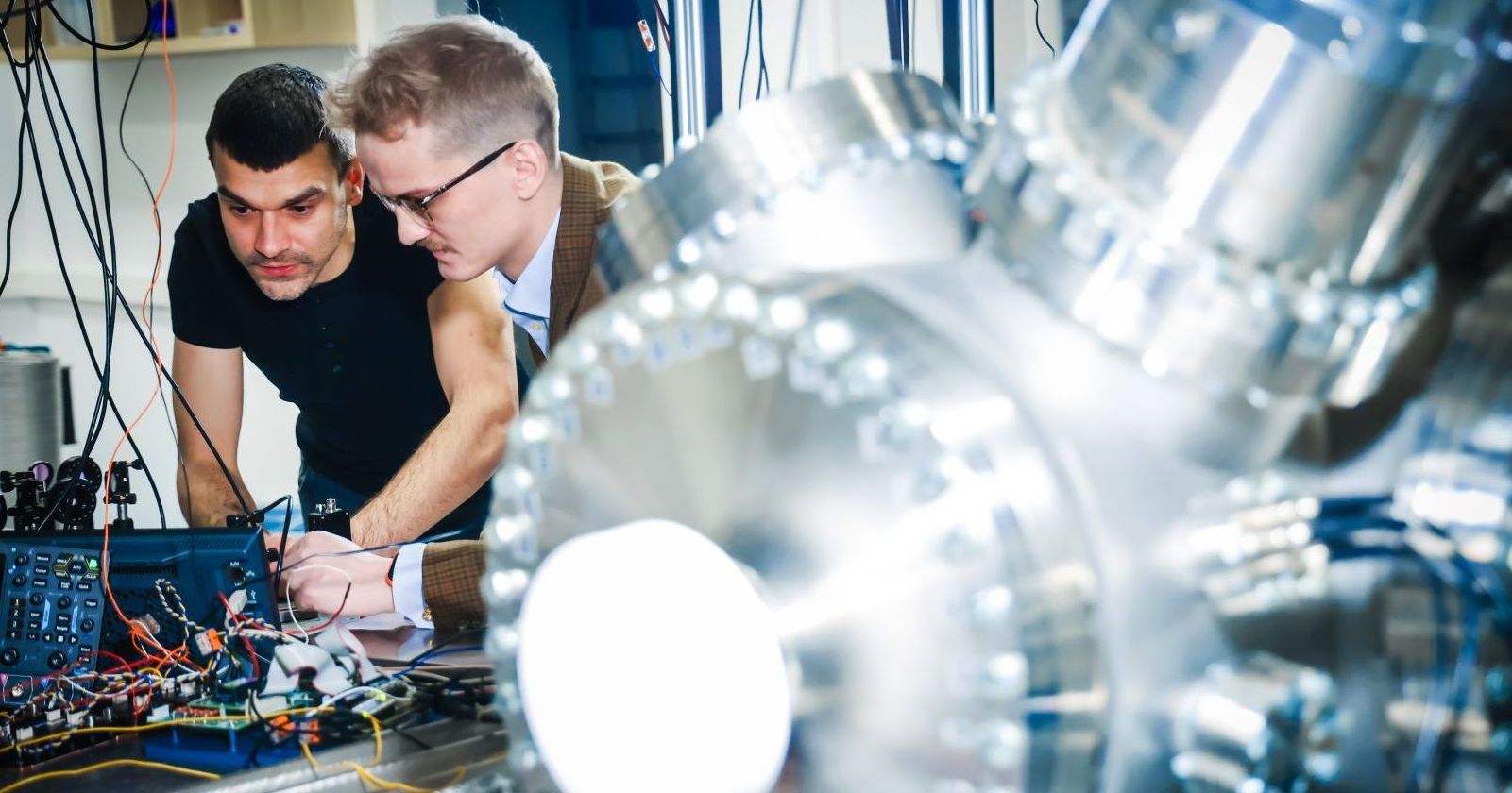 Two men are working in a laboratory. There are many cables in the background