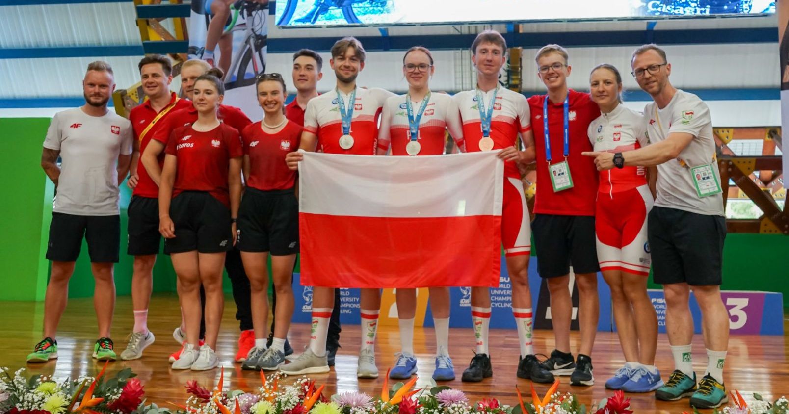 Reprezentacja Polski na Akademickich Mistrzostwach Świata w kolarstwie szosowym zdobyła sześć medali Na zdjęciu stoi akademicka reprezentacja Polski w kolarstwie szosowym z medalami na szyjach i polską flagą w rękach