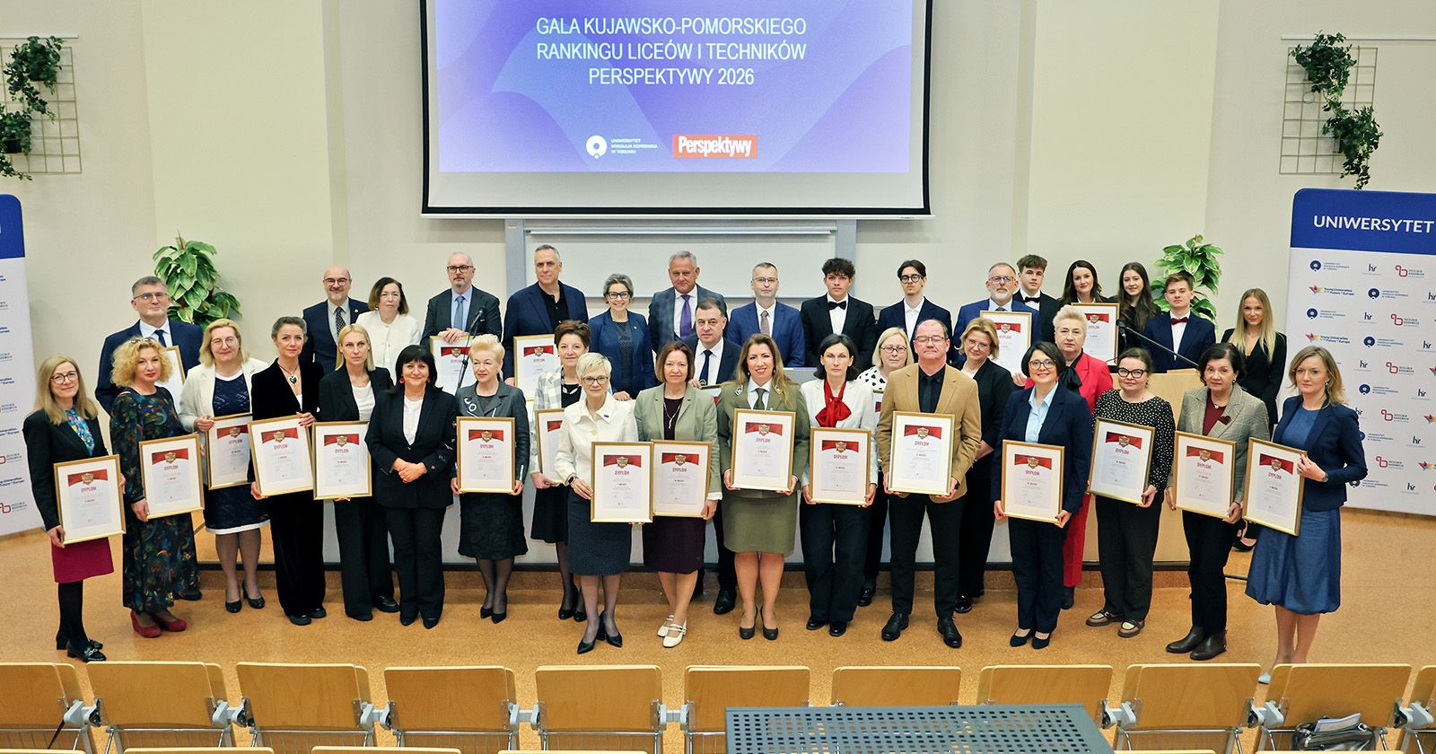 Zdjęcie grupowe, ludzie stoją eksponując dyplomy, w tle ekran z napisem Gala Kujawsko-Pomorskiego Rankingu Liceów i Techników Perspektywy 2026