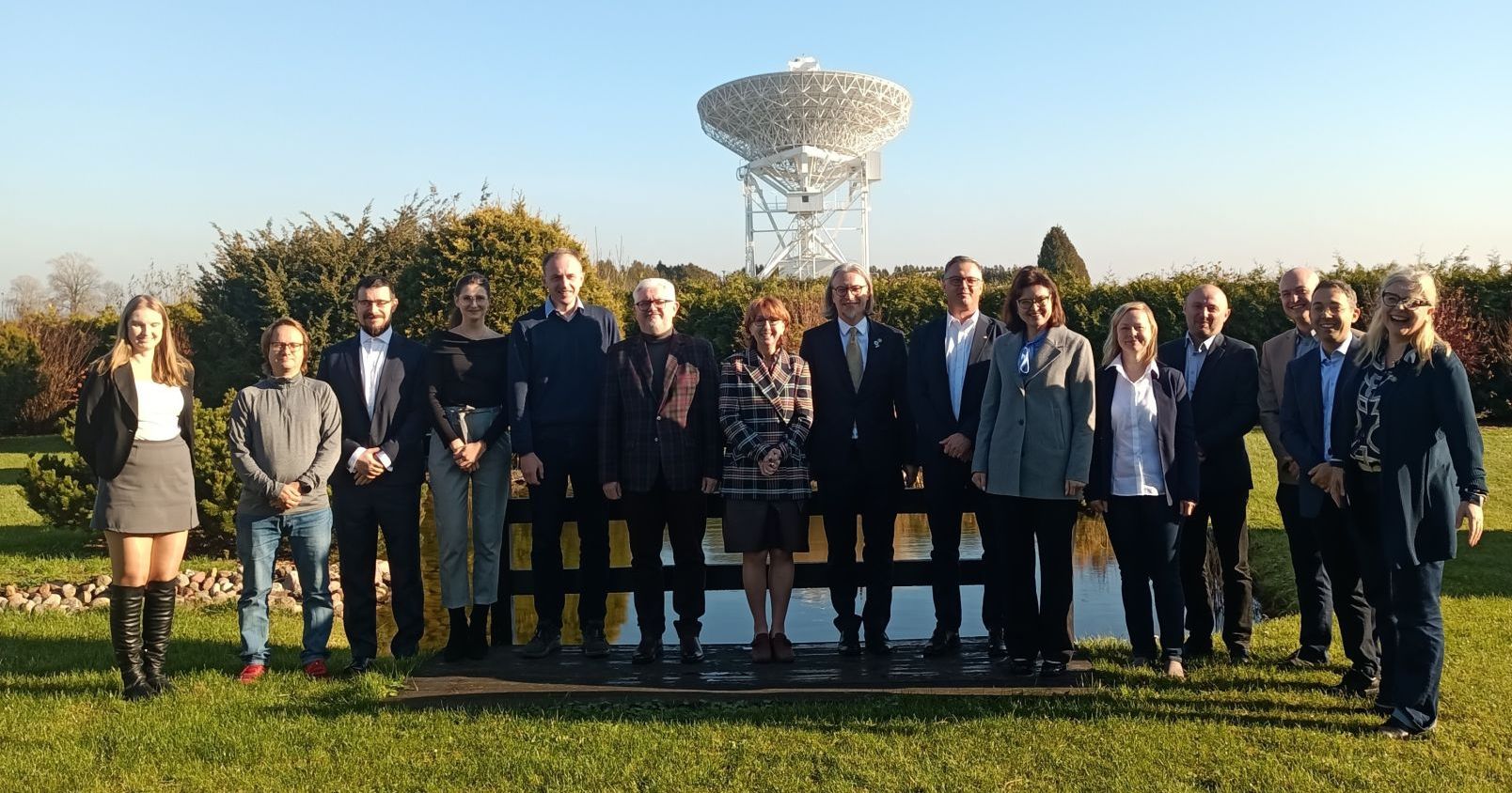 Kilkanaście osób stoi w rzędzie na zewnątrz, w tle widać radioteleskop znajdujący się w obserwatorium astronomicznym UMK w Piwnicach