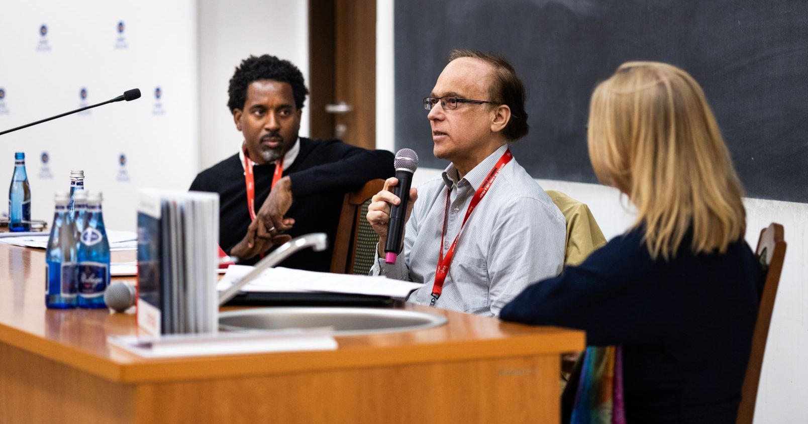 Jason Jackson, Jorge Esquirol, and Joanna Modrzyńska are seated at the head table in Darwin Hall. Jorge Esquirol speaks into the microphone