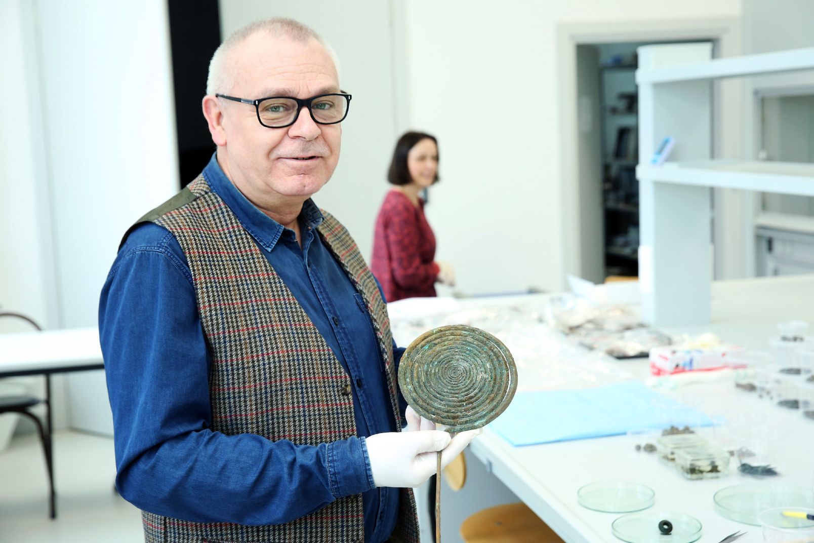 Prof. Jacek Gackowski stoi z jedną ze ślimakowatych ozdób prehistorycznych w ręku odnalezionych na Pojezierzu Chełmińskim