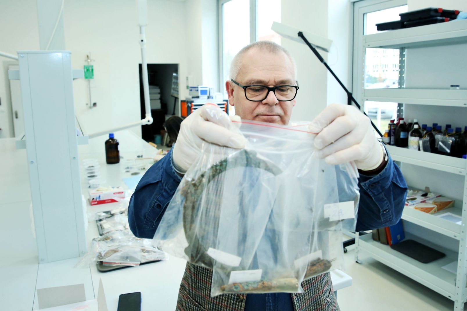 Prof. Jacek Gackowski trzyma w rękach woreczki z artefaktami odkrytymi na Pojezierzu Chełmińskim