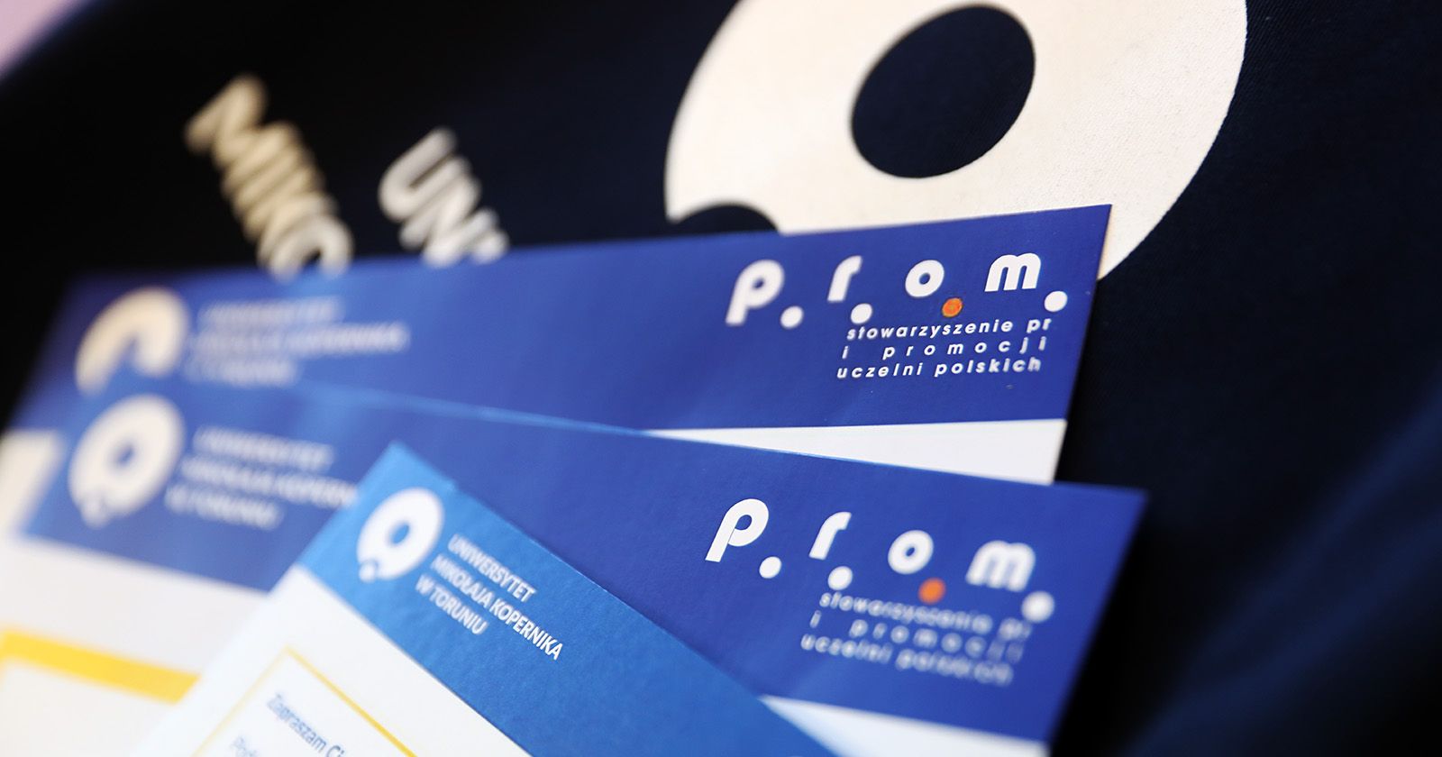 Na zdjęciu widać fragmenty trzech zaproszeń na konferencję PRom i logo UMK