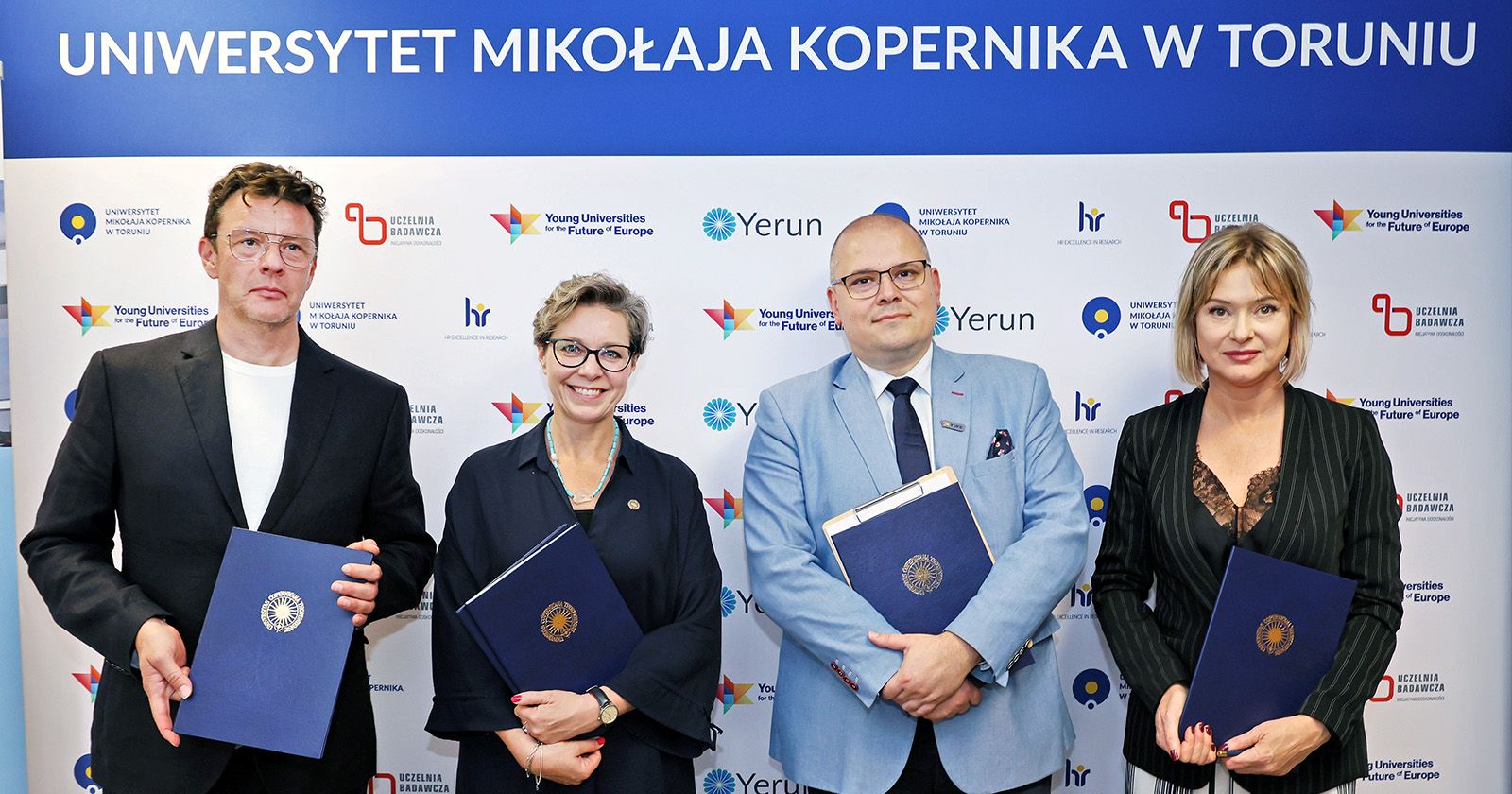 Prorektorzy i przedstawiciele firm architektonicznych pozują do zdjęcia po podpisaniu umów. W rękach trzymają teczki.