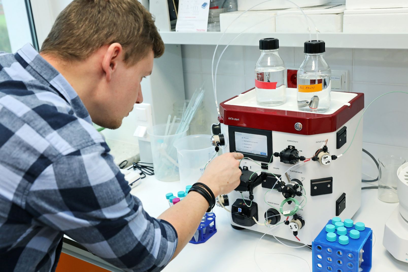Mgr Mateusz Kwiatkowski stoi przy chromatografie cieczowym do oczyszczania białek