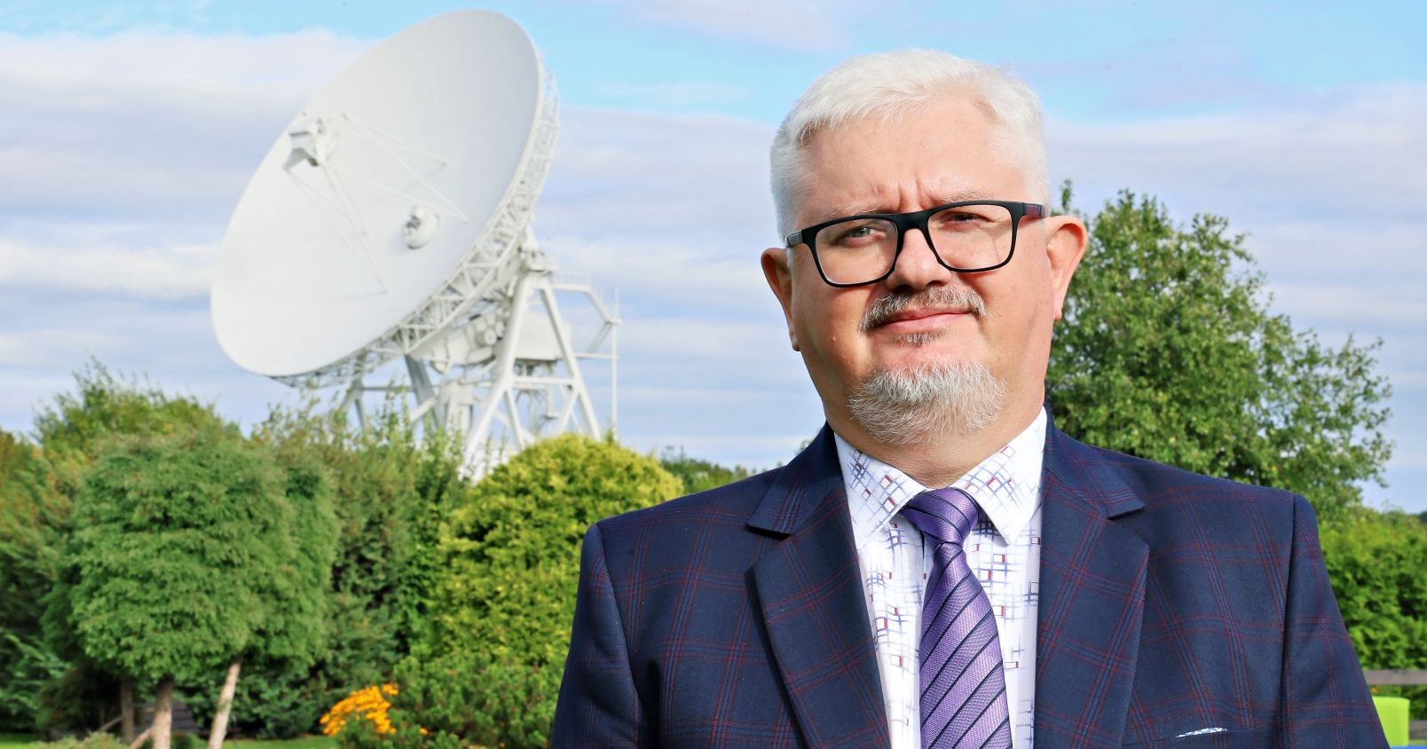 Profesor Krzysztof Katarzyński stoi na tle czaszy radioteleskopu w podtoruńskich Piwnicach