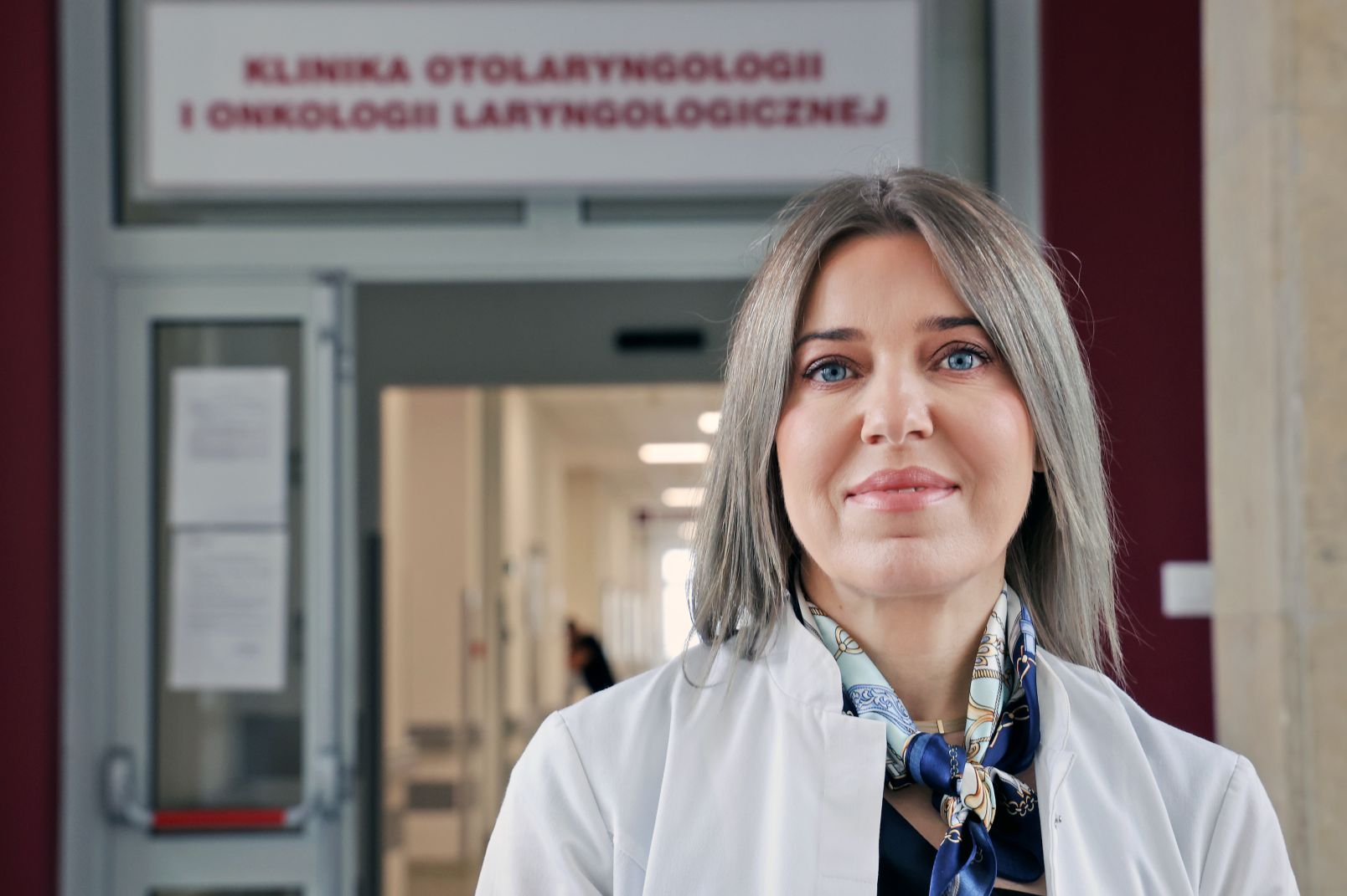 Portret prof. Nowaczewskiej na tle drzwi prowadzących do Kliniki Otolaryngologii i Onkologii Laryngologicznej