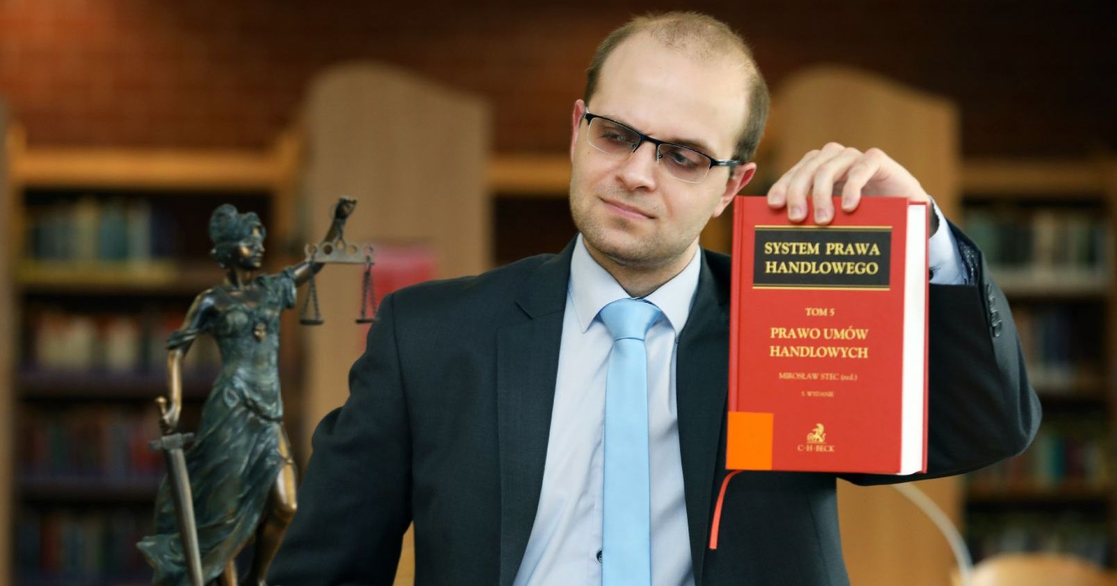 Dr Marcin Drewek z Wydziału Prawa i Administracji UMK trzyma w ręku książkę "Prawo umów handlowych"