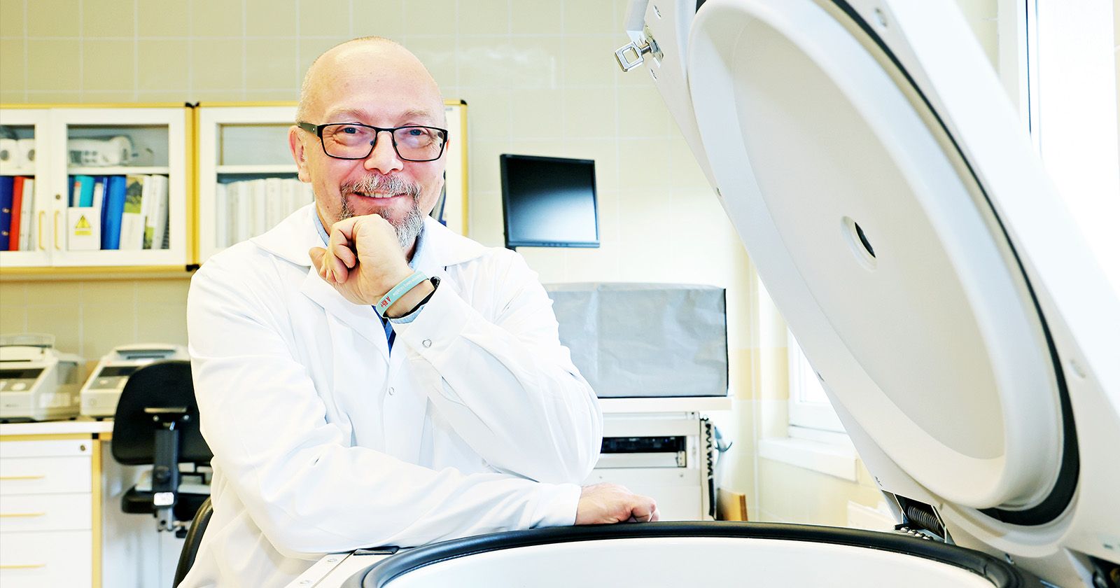 Prof. Marcin Woźniak w białym fartuchu w laboratorium przy jakimś urządzeniu z dużą okrągłą pokrywką