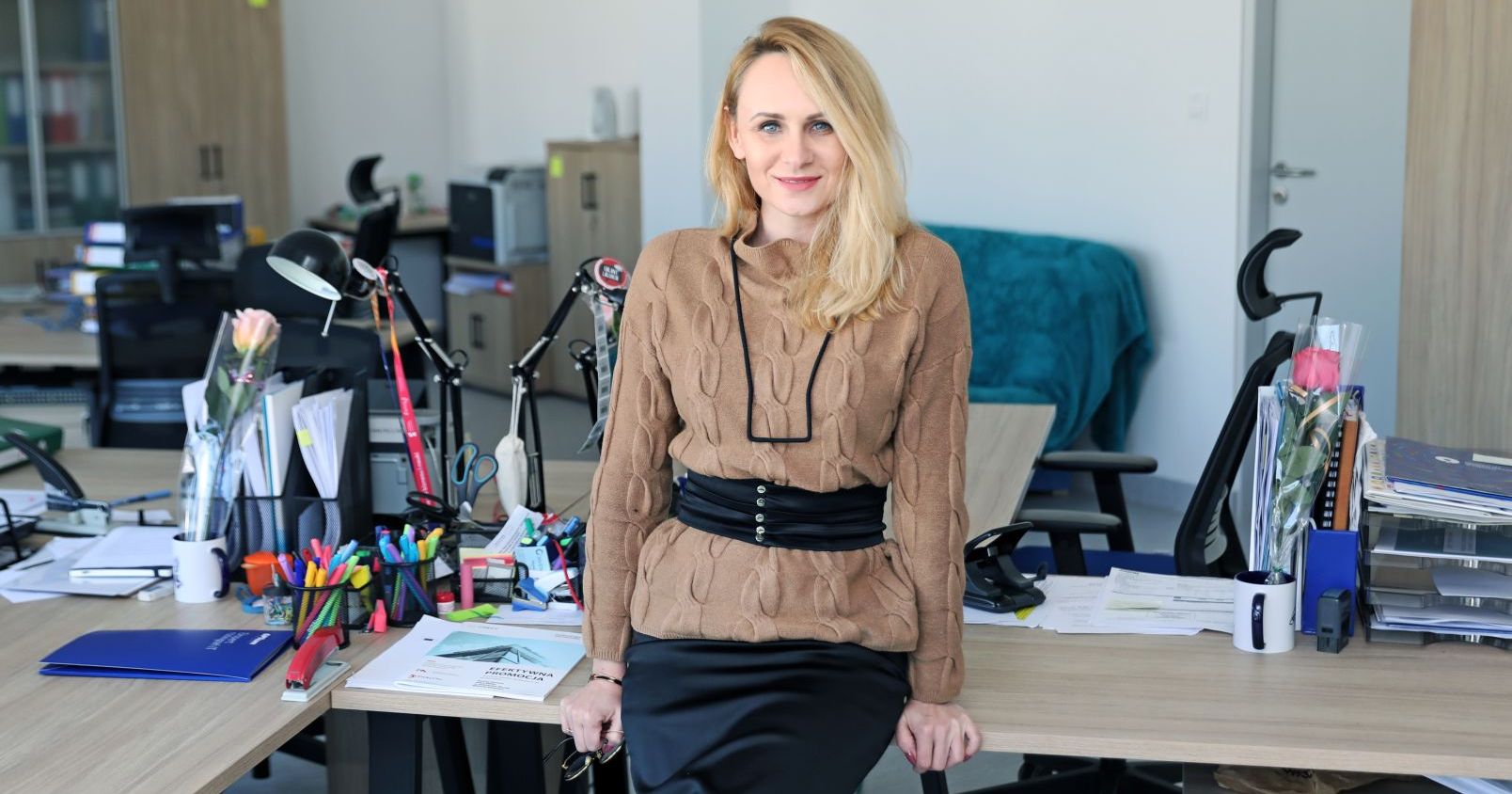 Dr Marlena Krohn, prezes Startova.pl Kobieta opiera się o biurko w biurze, pozuje do zdjęcia.