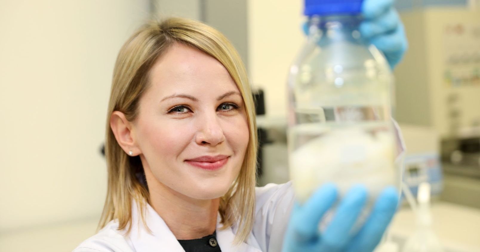 Prof. Marta Pokrywczyńska trzyma przed sobą szklaną butelkę z preparatem, patrzy w obiektyw i się uśmiecha