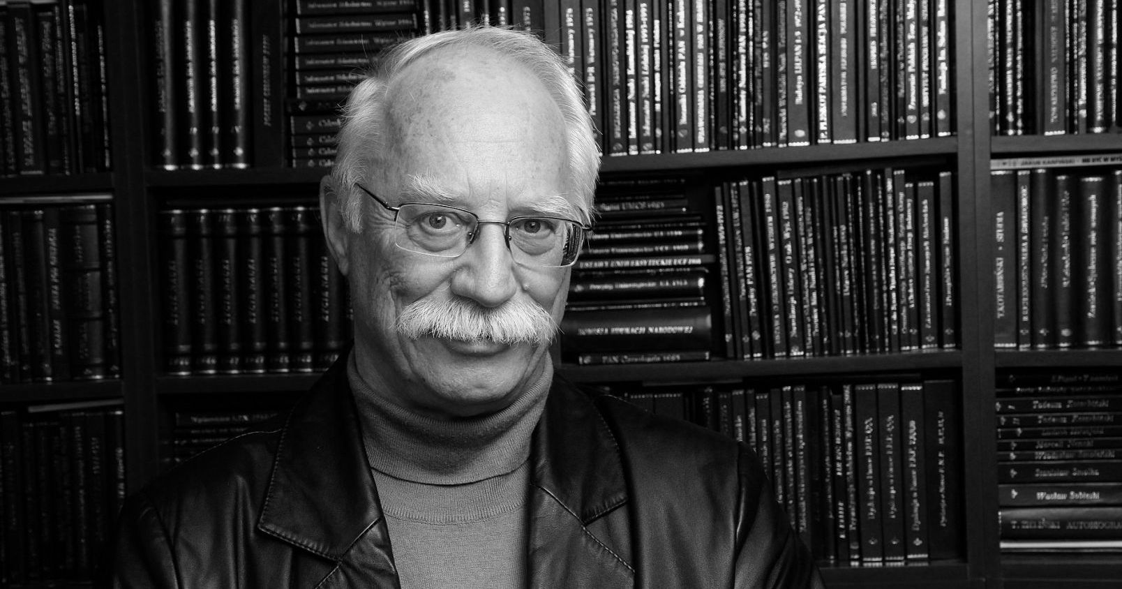  Portret prof. Piotra Hübnera na tle biblioteczki z książkami