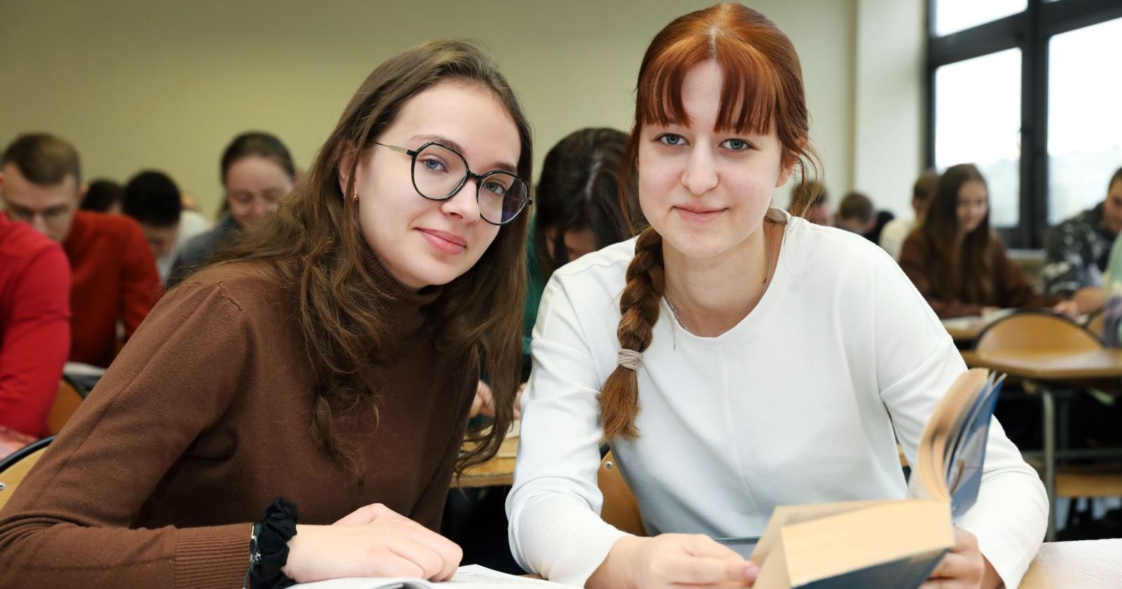 Z rabatu na kursy językowe mogą skorzystać wszyscy mieszkańcy Torunia i okolic Dwie dziewczyny siedzą w ławce, jedna trzyma otwartą książkę, obie patrzą w obiektyw