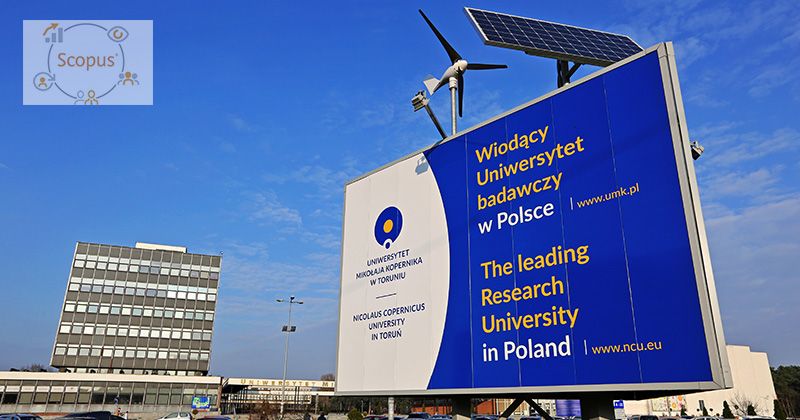  Zdjęcie przedstawia bilbord z logo UMK i napisem "wiodący uniwersytet badawczy w Polsce". W tle widać budynek rektoratu i auli UMK. W lewym górnym rogu nałożone jest logo rankingu Scopus.