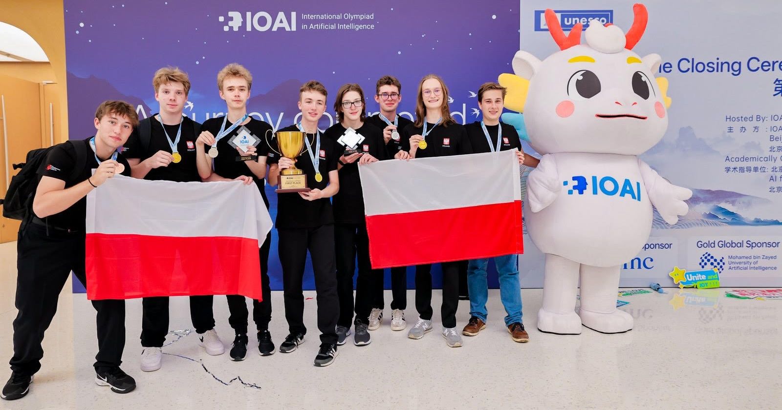 Oba zespoły, które reprezentowały Polskę podczas IOAI, znalazły się na podium konkursu drużynowego Osiem osób (dwie drużyny) pozują do zdjęcia z dwiema flagami Polski i oficjalną maskotką Olimpiady